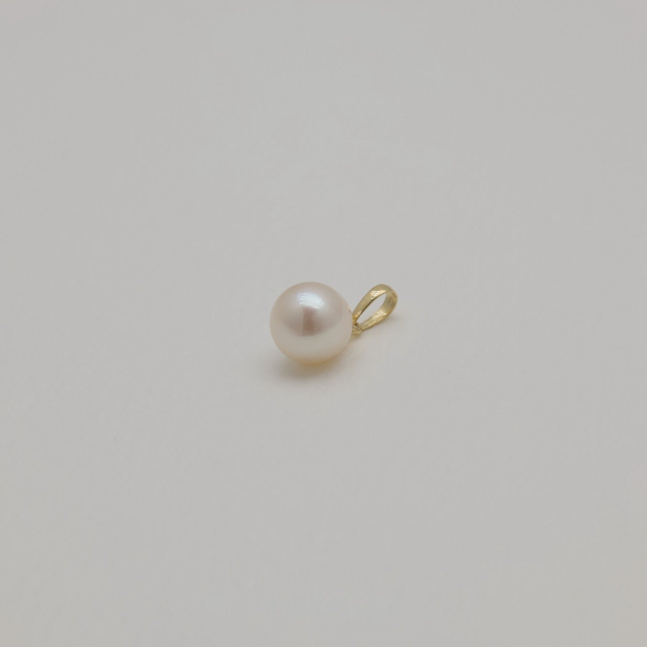 Minimalist gold and pearl pendant photographed from distance on cream backdrop