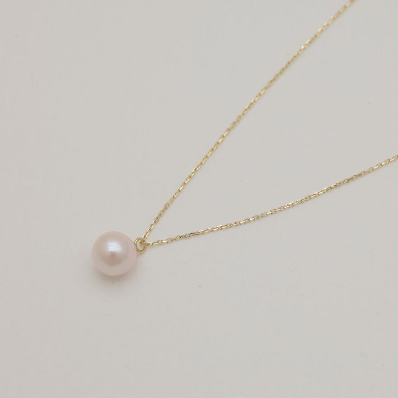 Elegant Akoya pearl pendant on a fine 10K gold chain, softly curved on a neutral backdrop.