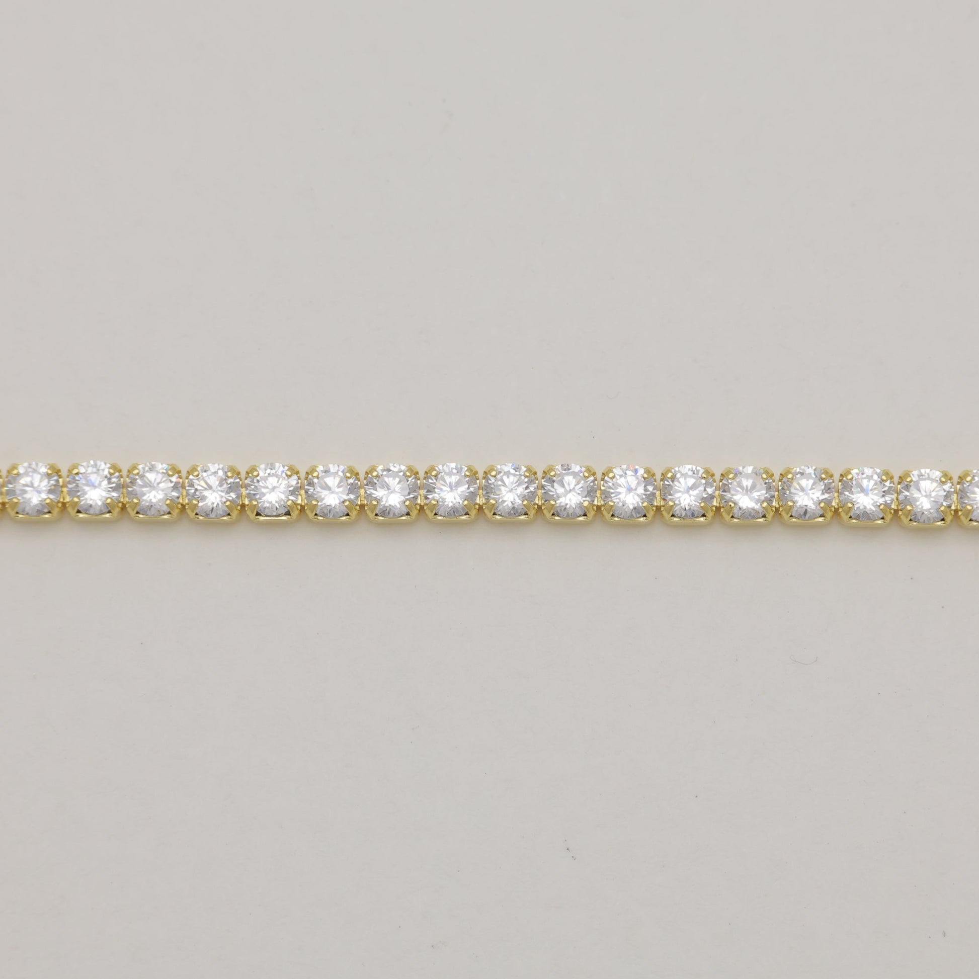 Gold bracelet with clear stones on a light gray background