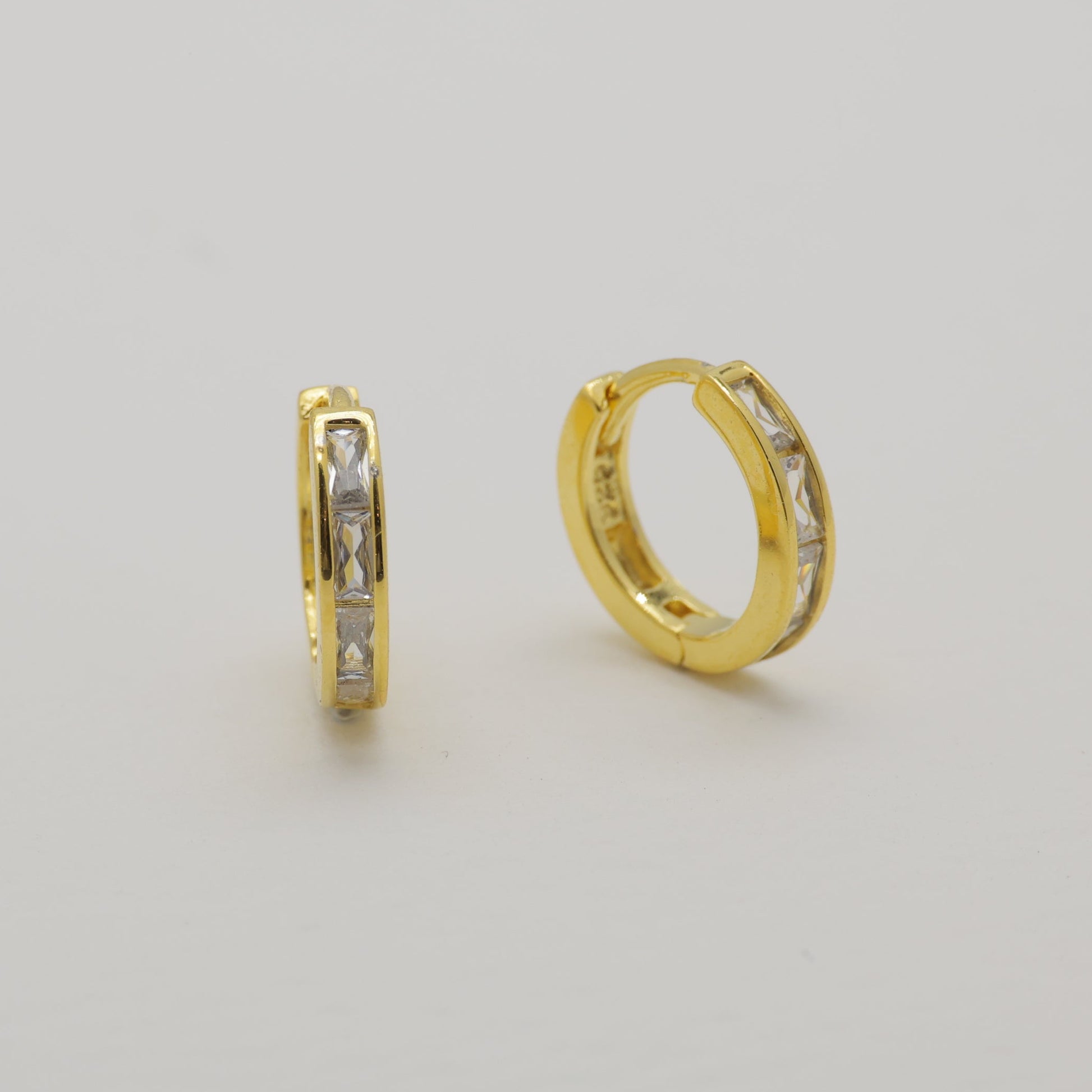 Gold hoop earrings with embedded stones on a light gray background