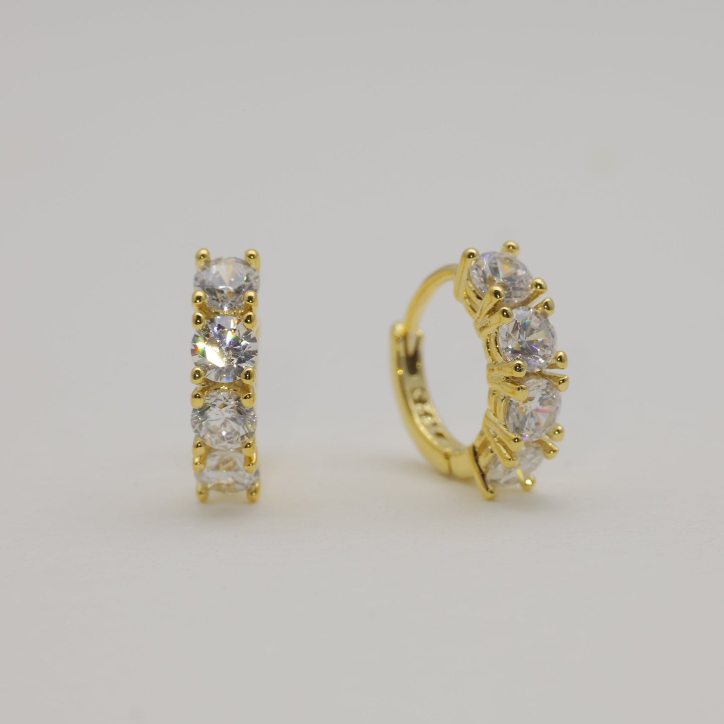 Gold hoop earrings with clear stones on a light gray background