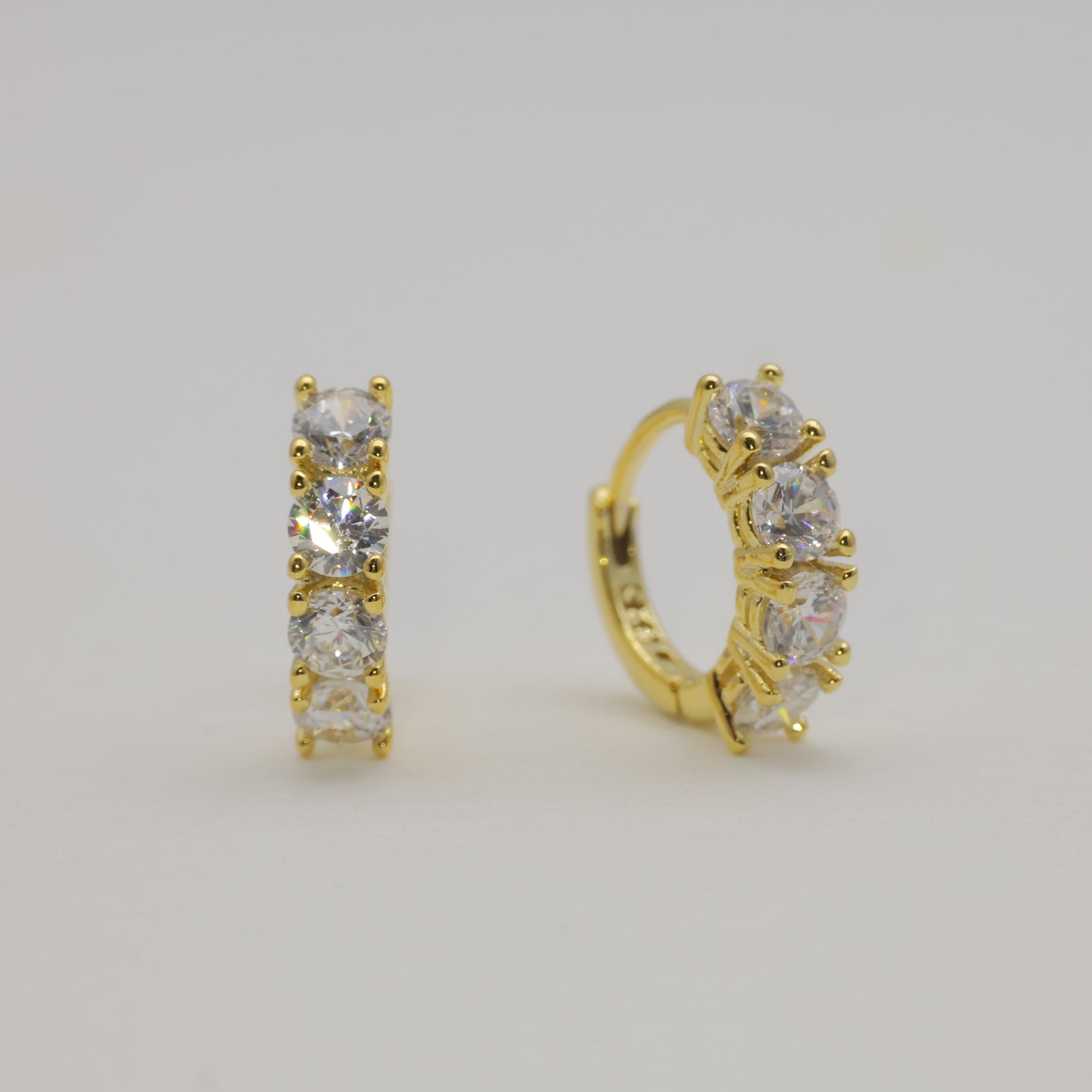 Gold hoop earrings with clear stones on a light gray background