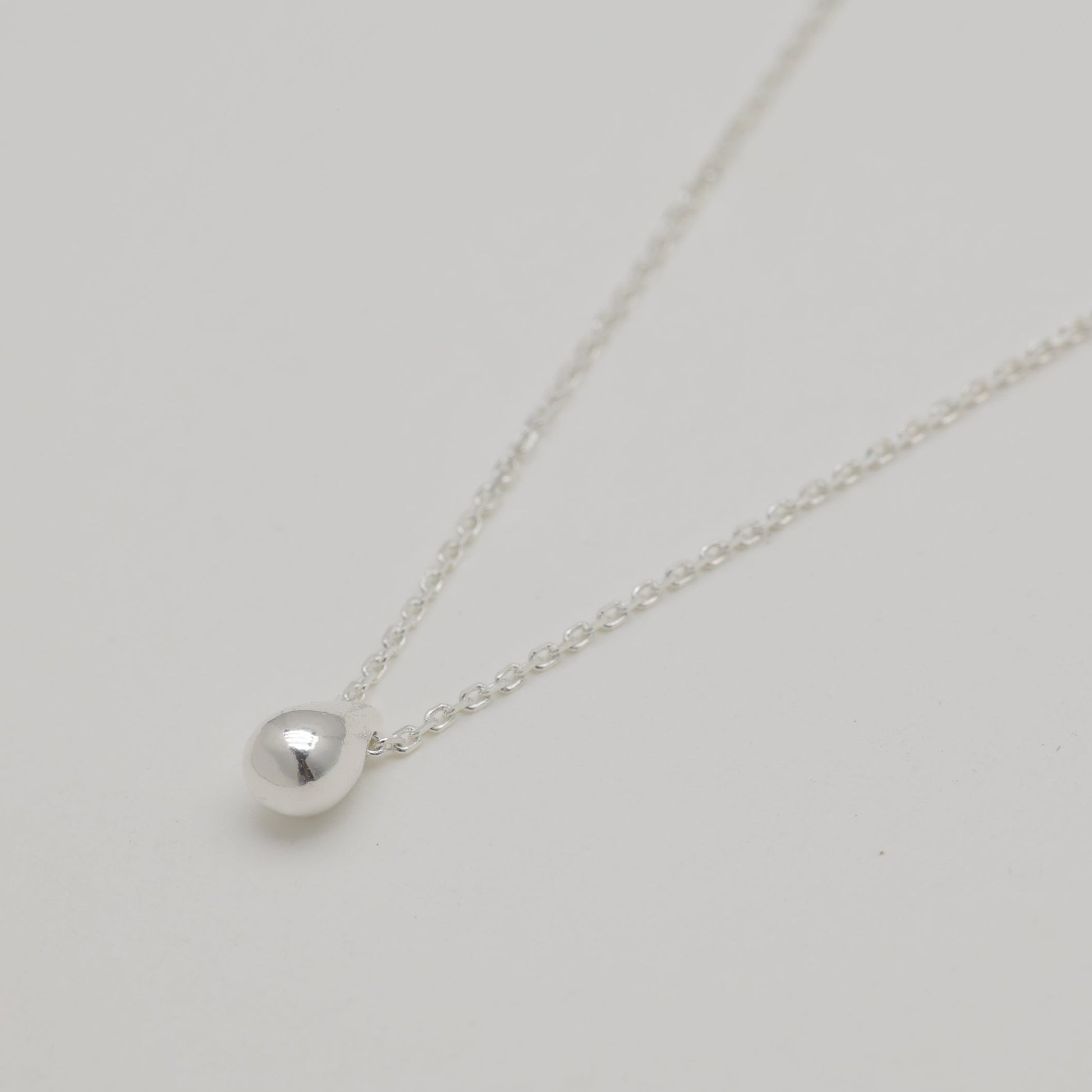 Angled view of polished silver teardrop pendant necklace.