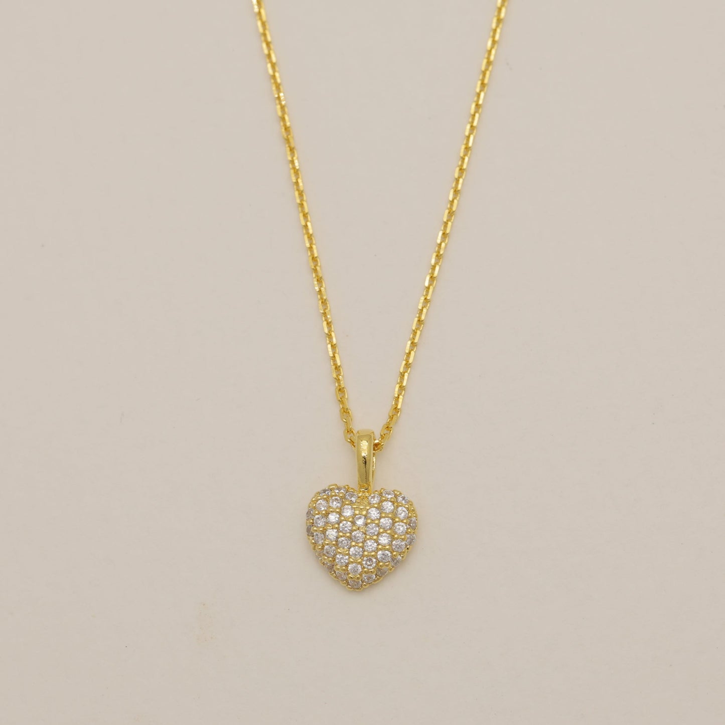 Gold heart-shaped pendant necklace on a beige background