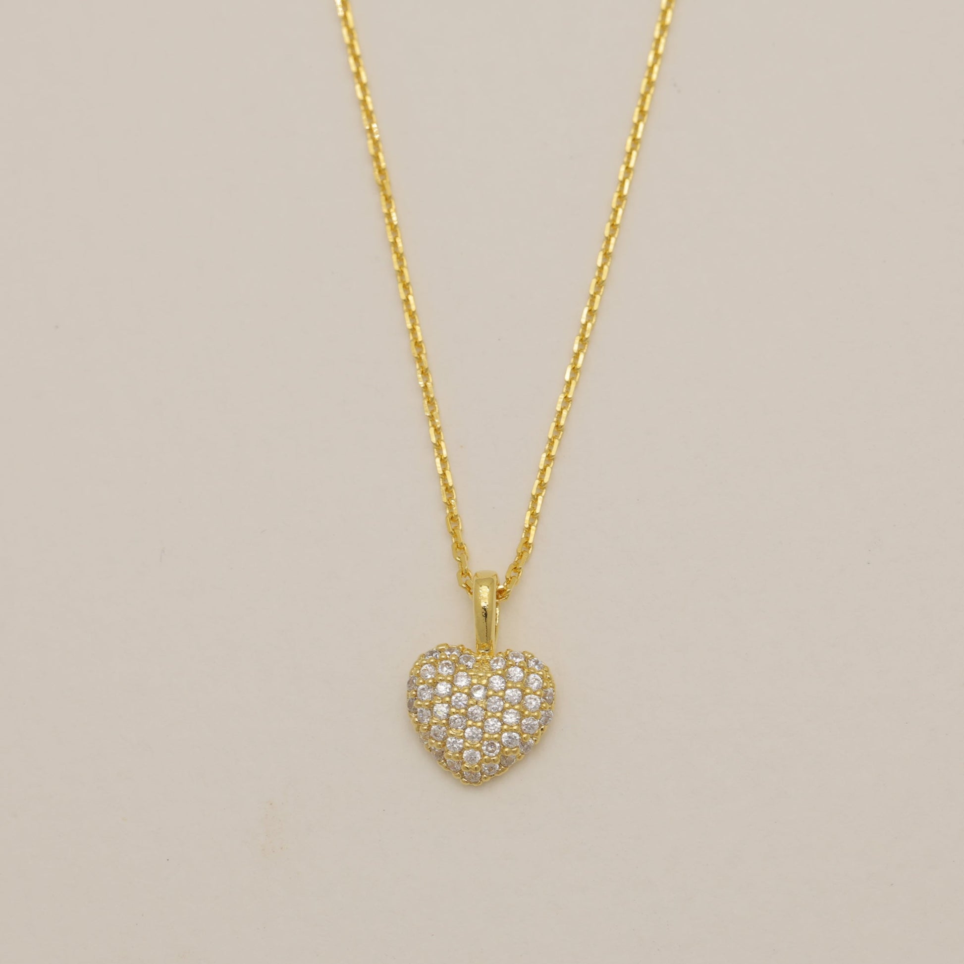 Gold heart-shaped pendant necklace on a beige background