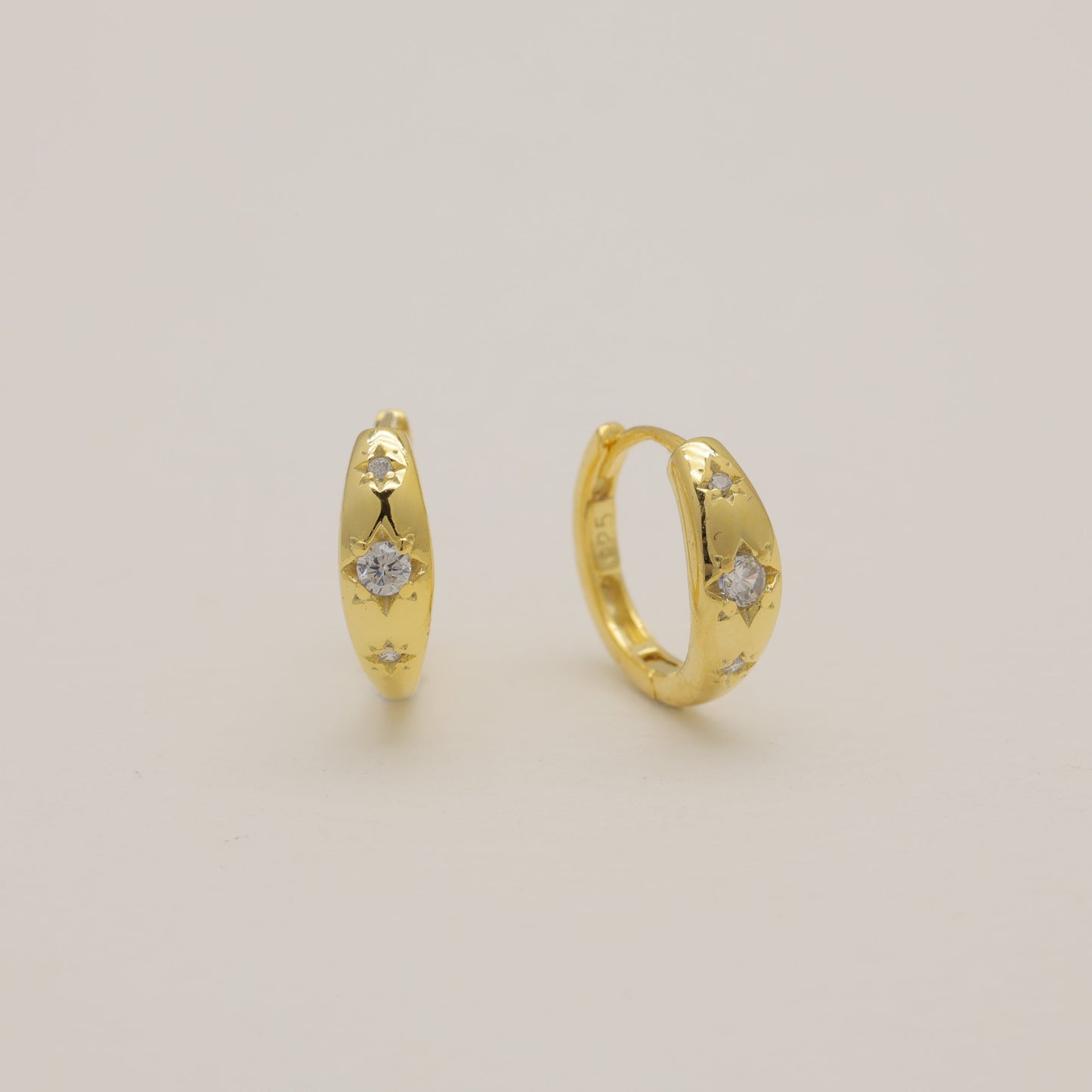 Pair of gold hoop earrings with small diamonds on a light beige background