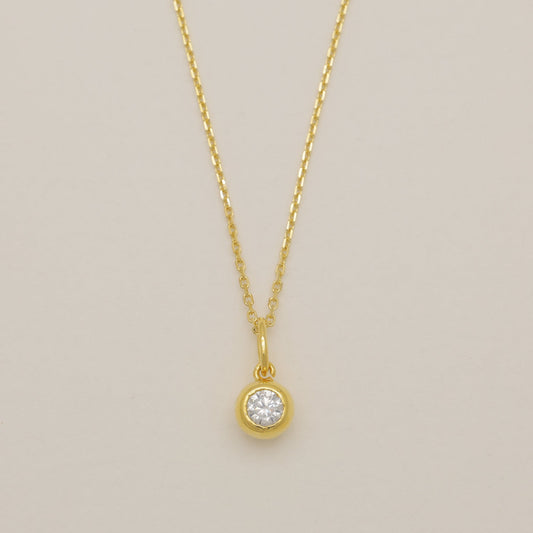 Gold necklace with a round pendant on a beige background