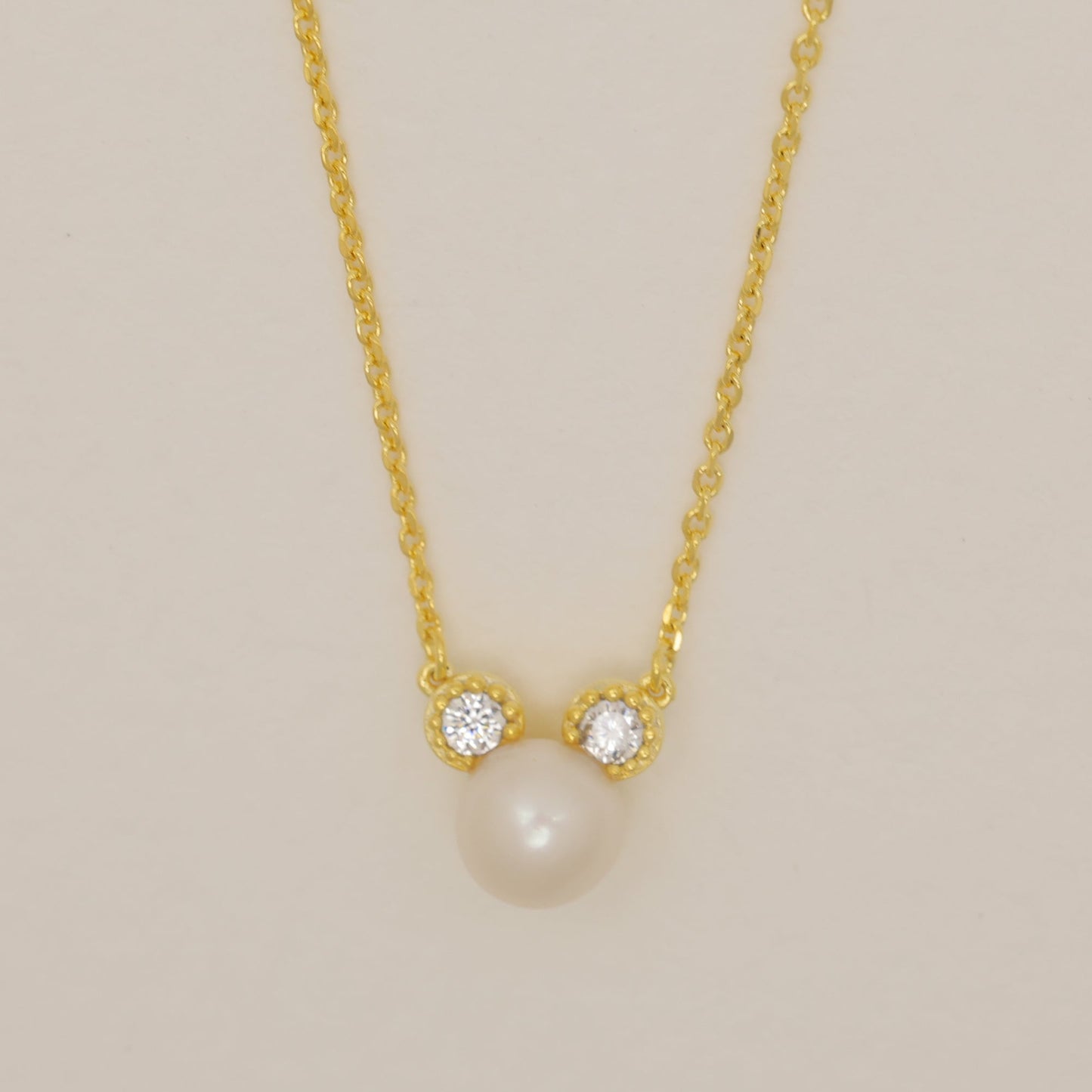 Gold necklace with a pearl pendant on a beige background
