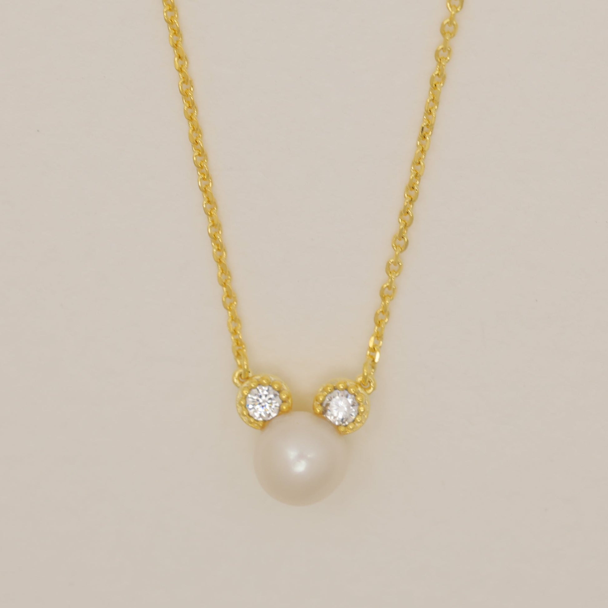 Gold necklace with a pearl pendant on a beige background