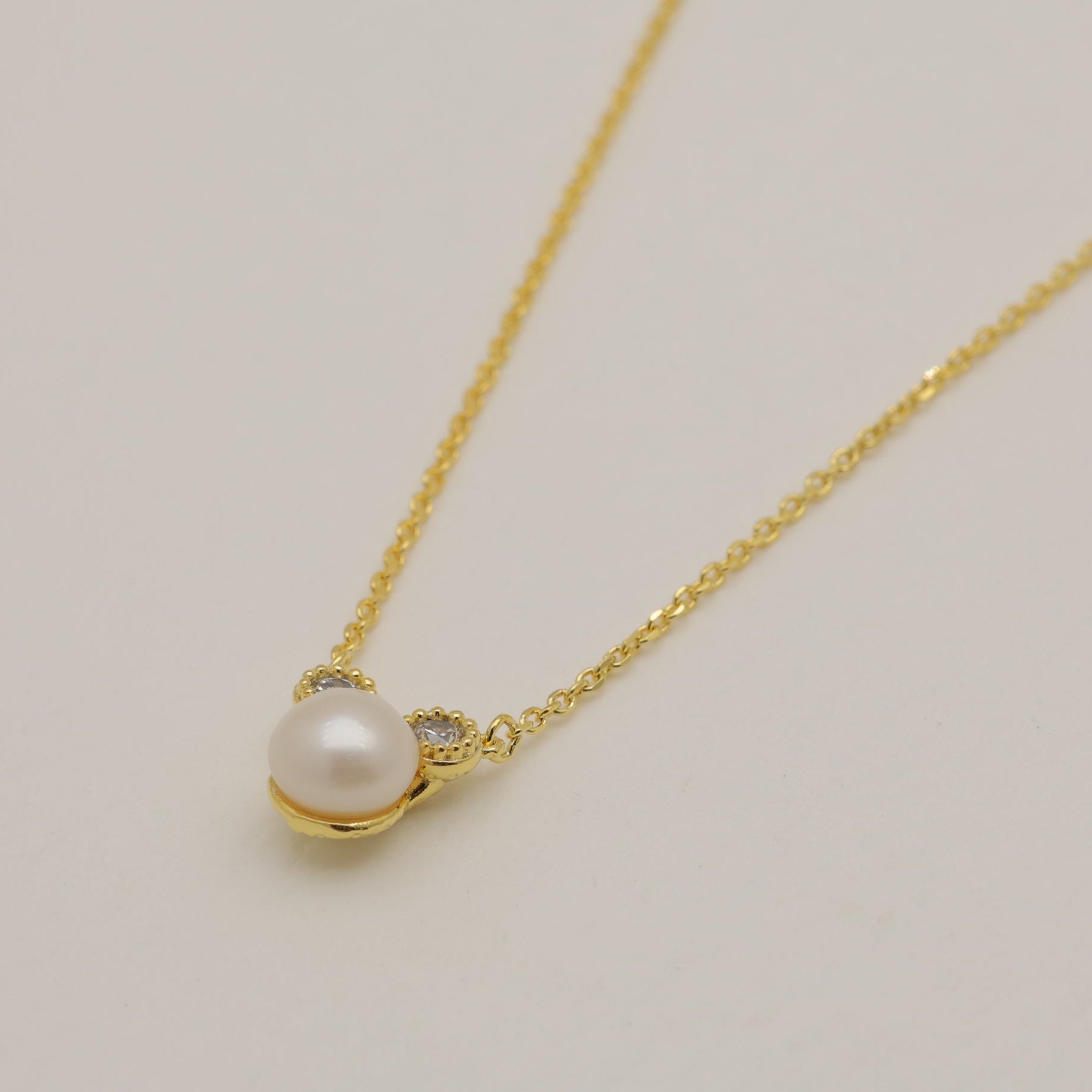 Gold necklace with a pearl pendant on a light beige background