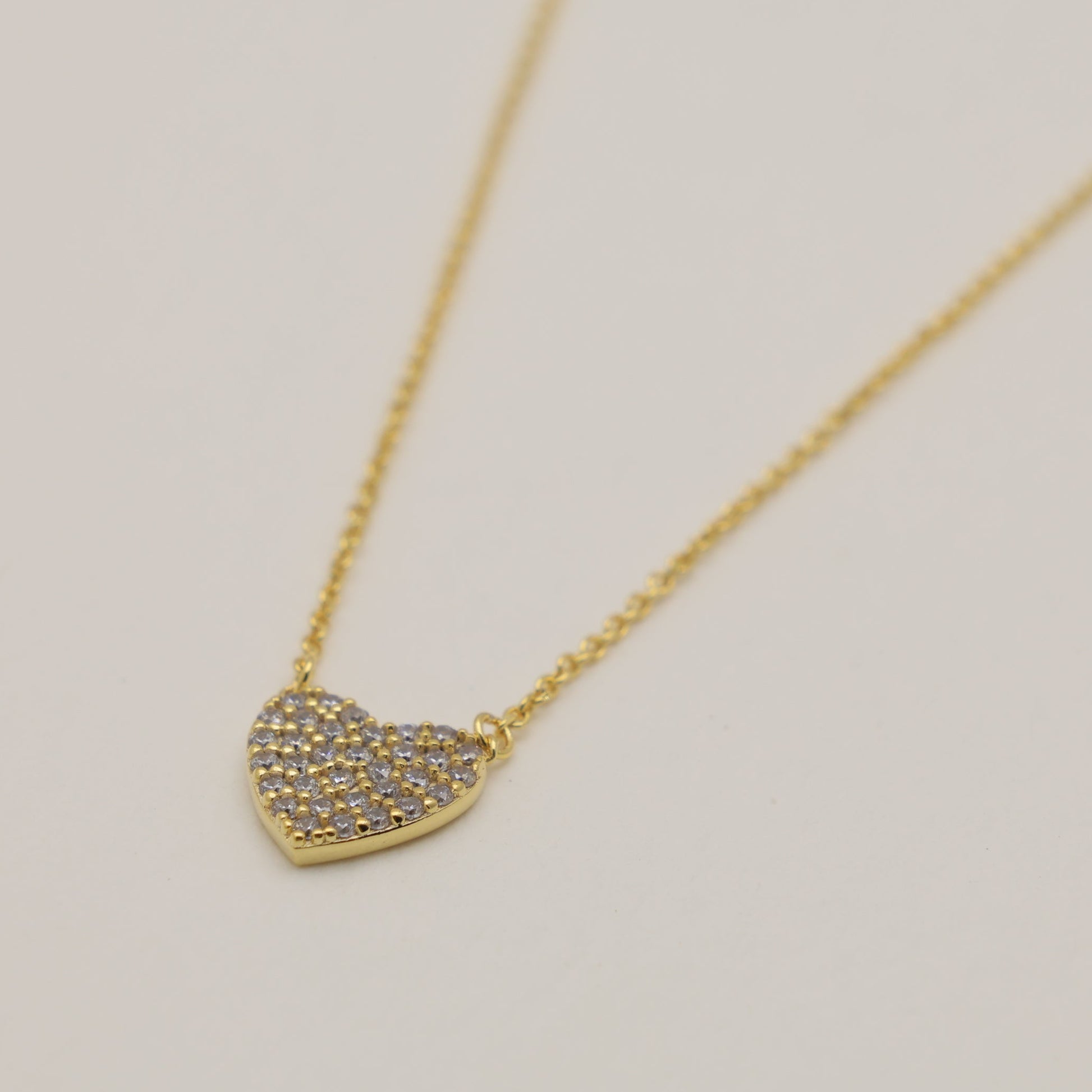Gold necklace with a heart-shaped pendant on a light gray background