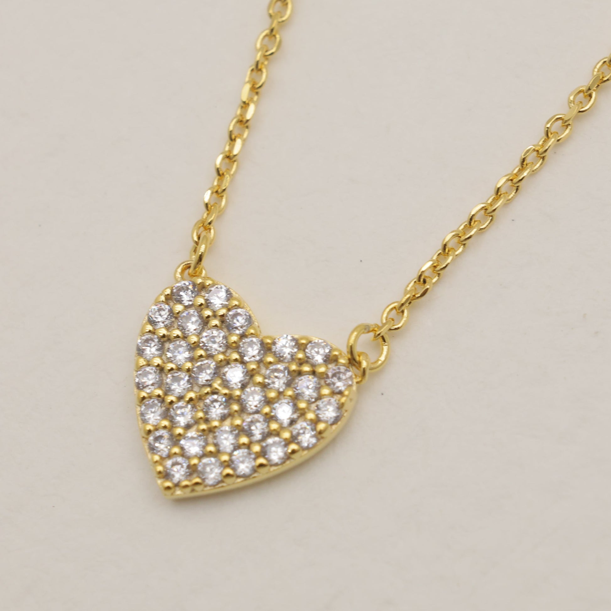 Gold heart-shaped necklace with clear stones on a beige background