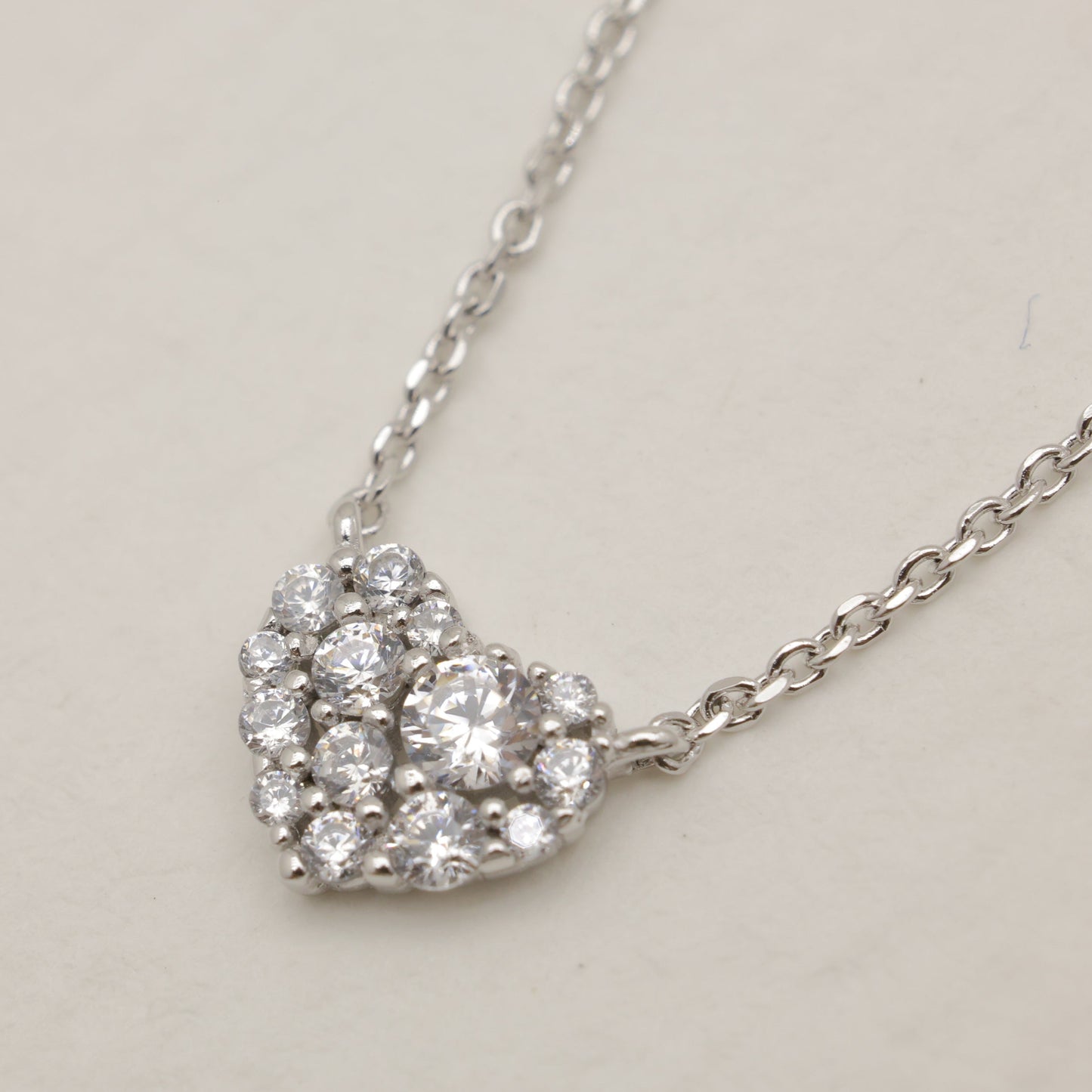Silver necklace with a heart-shaped diamond pendant on a light gray background