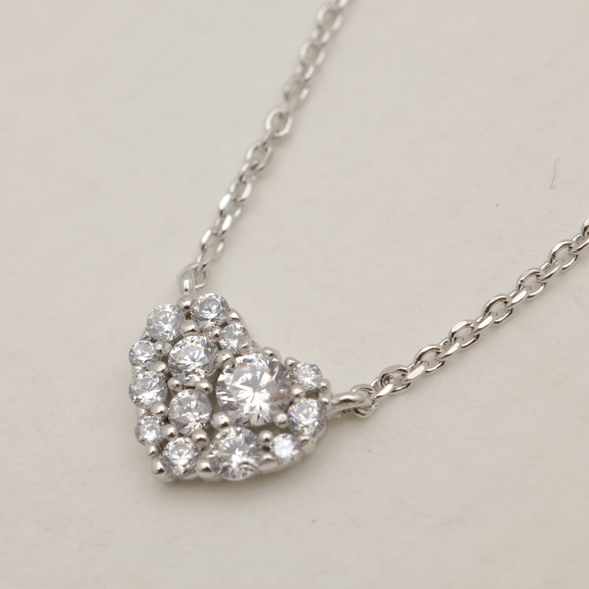 Silver necklace with a heart-shaped diamond pendant on a light gray background