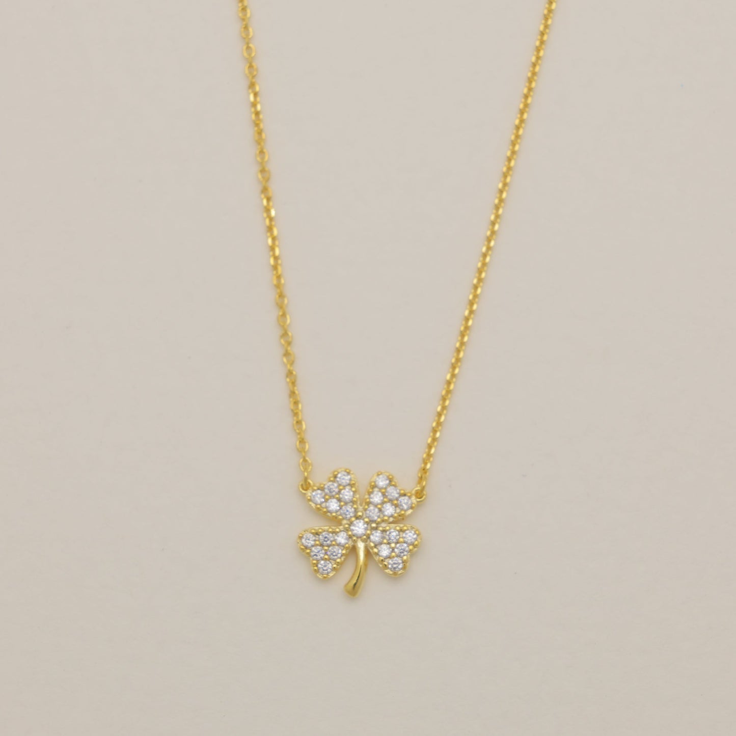 Gold necklace with a clover-shaped pendant on a beige background