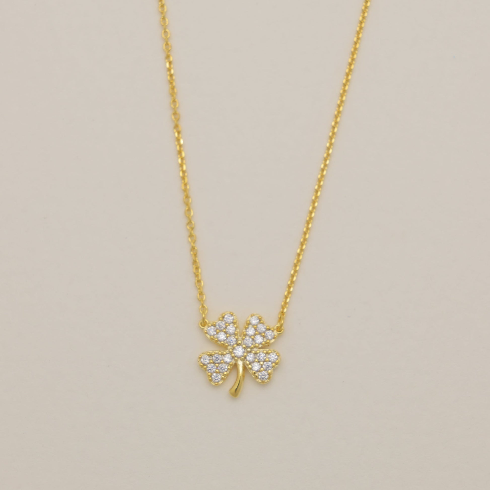 Gold necklace with a clover-shaped pendant on a beige background
