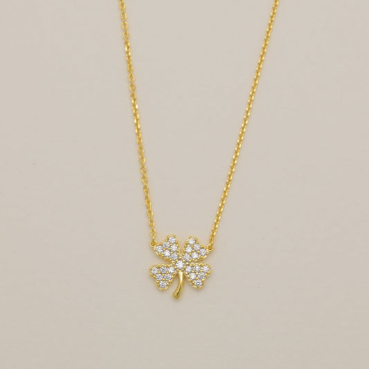 Gold necklace with a clover-shaped pendant on a beige background
