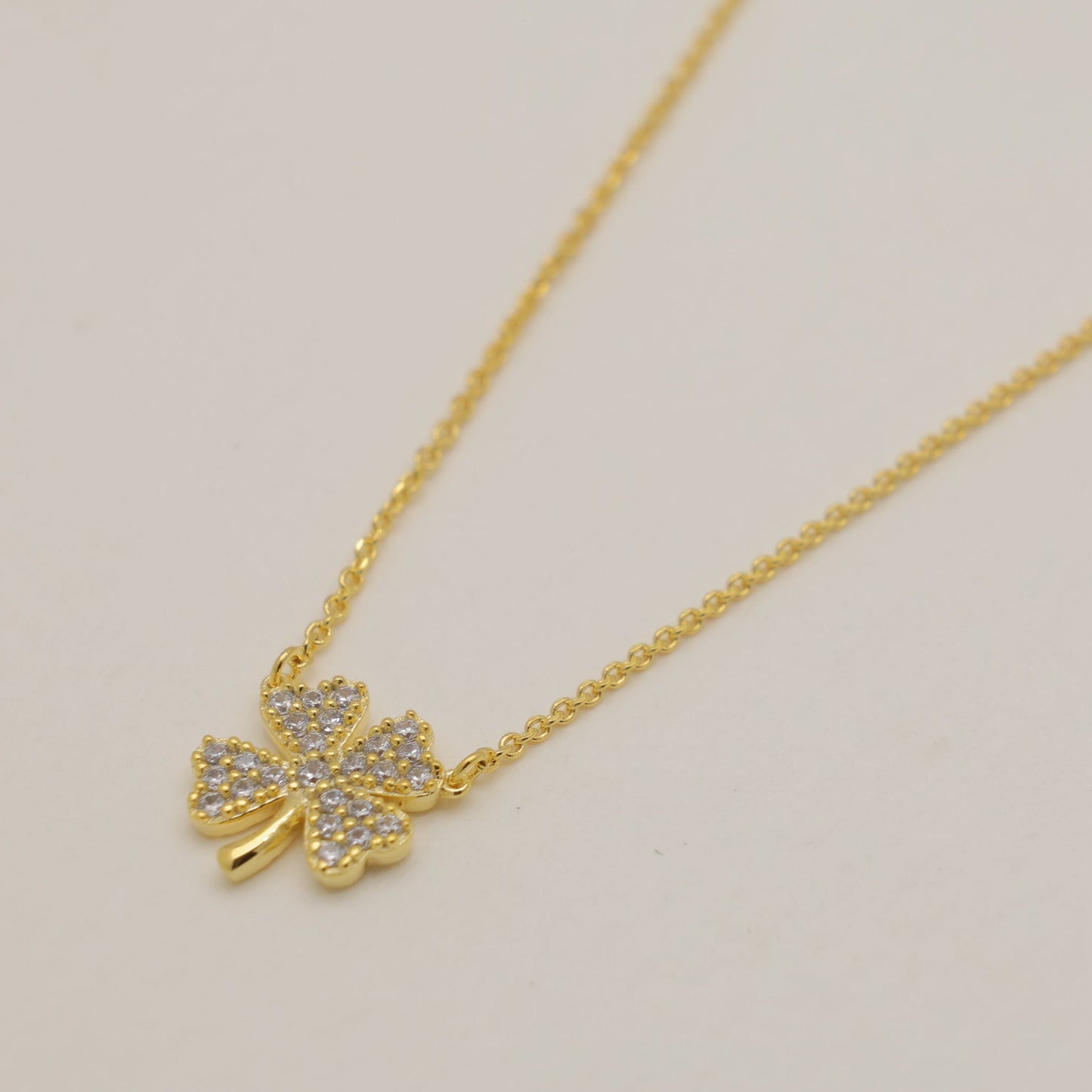 Gold necklace with a four-leaf clover pendant on a beige background