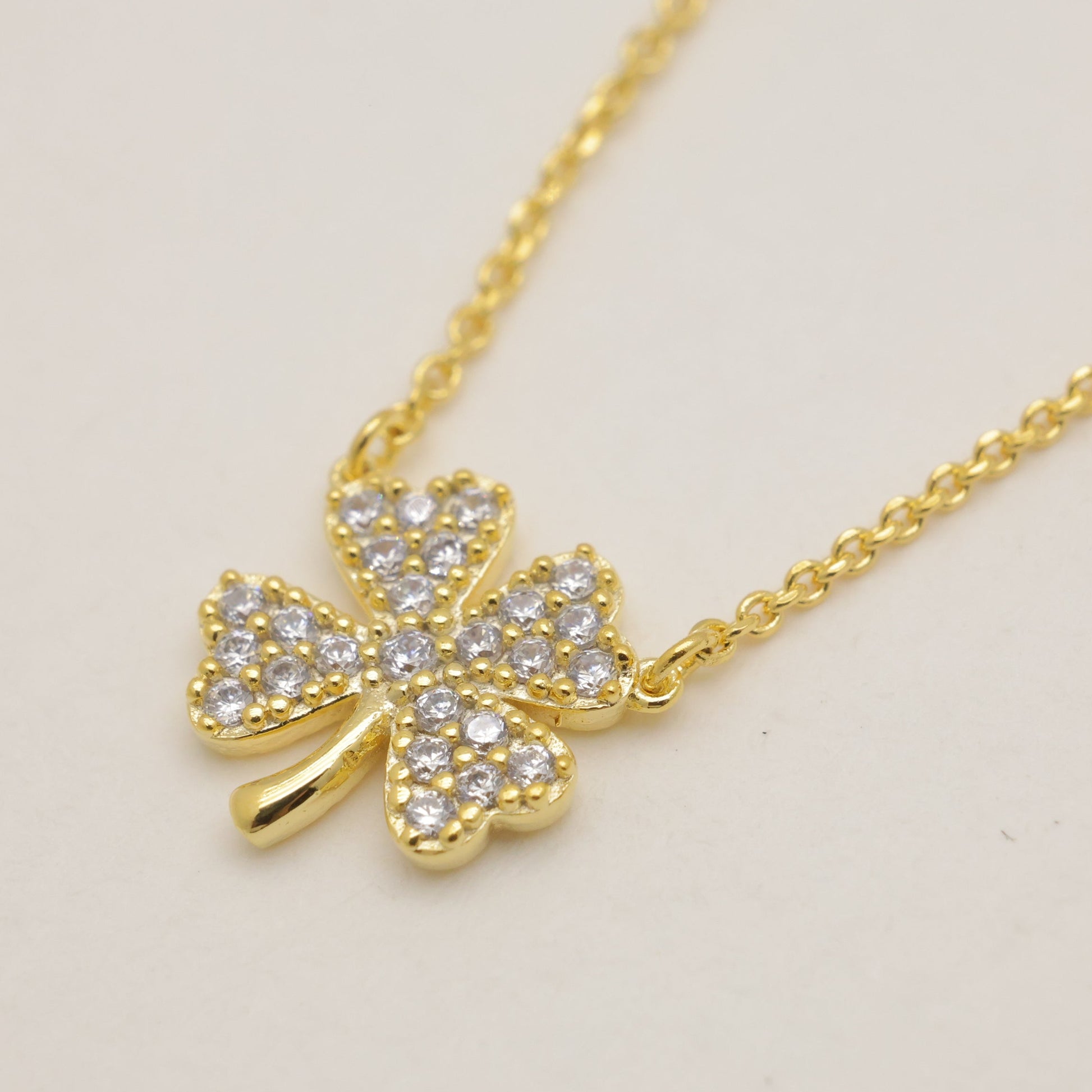 Gold necklace with a clover-shaped pendant on a light beige background