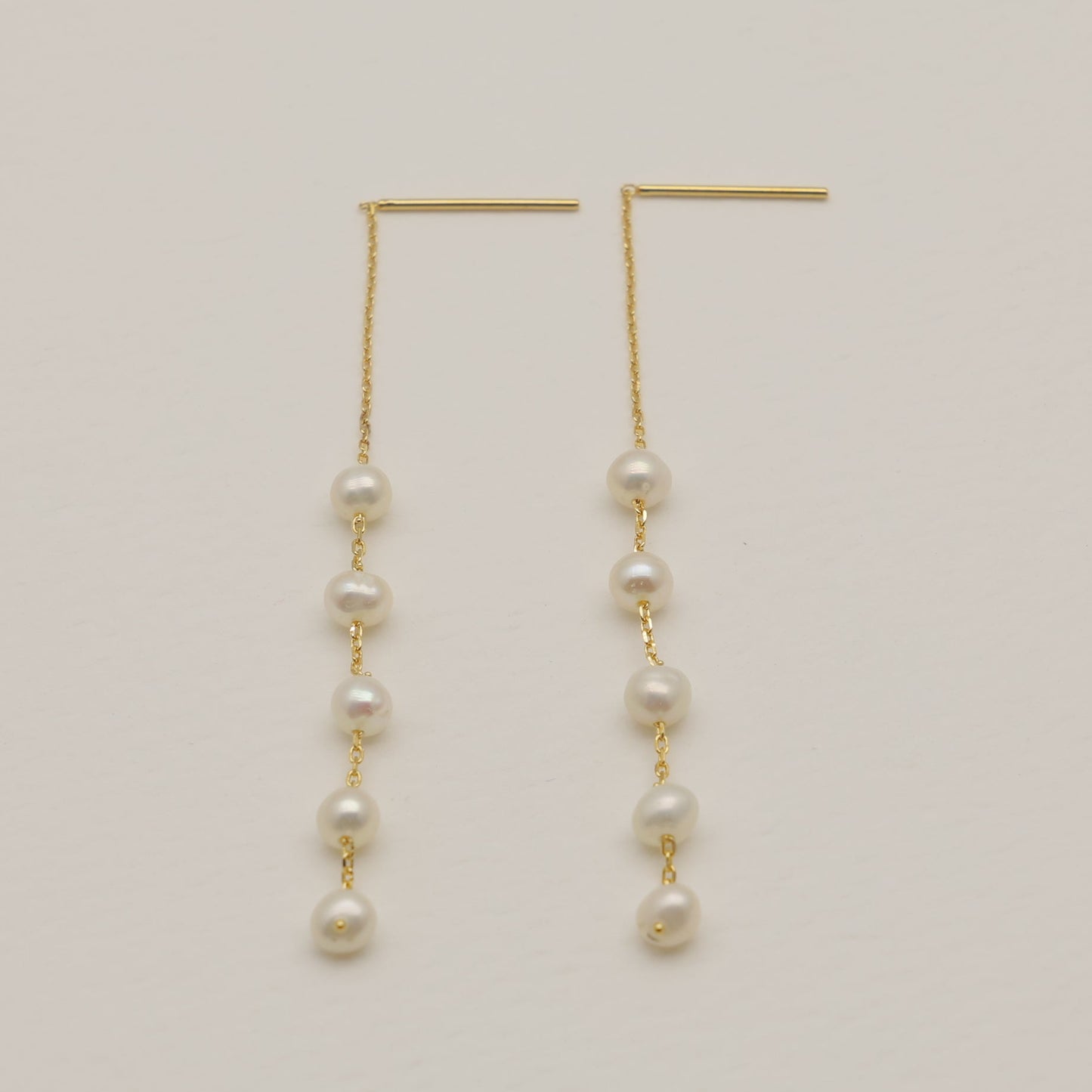 Gold earrings with pearl beads on a light beige background