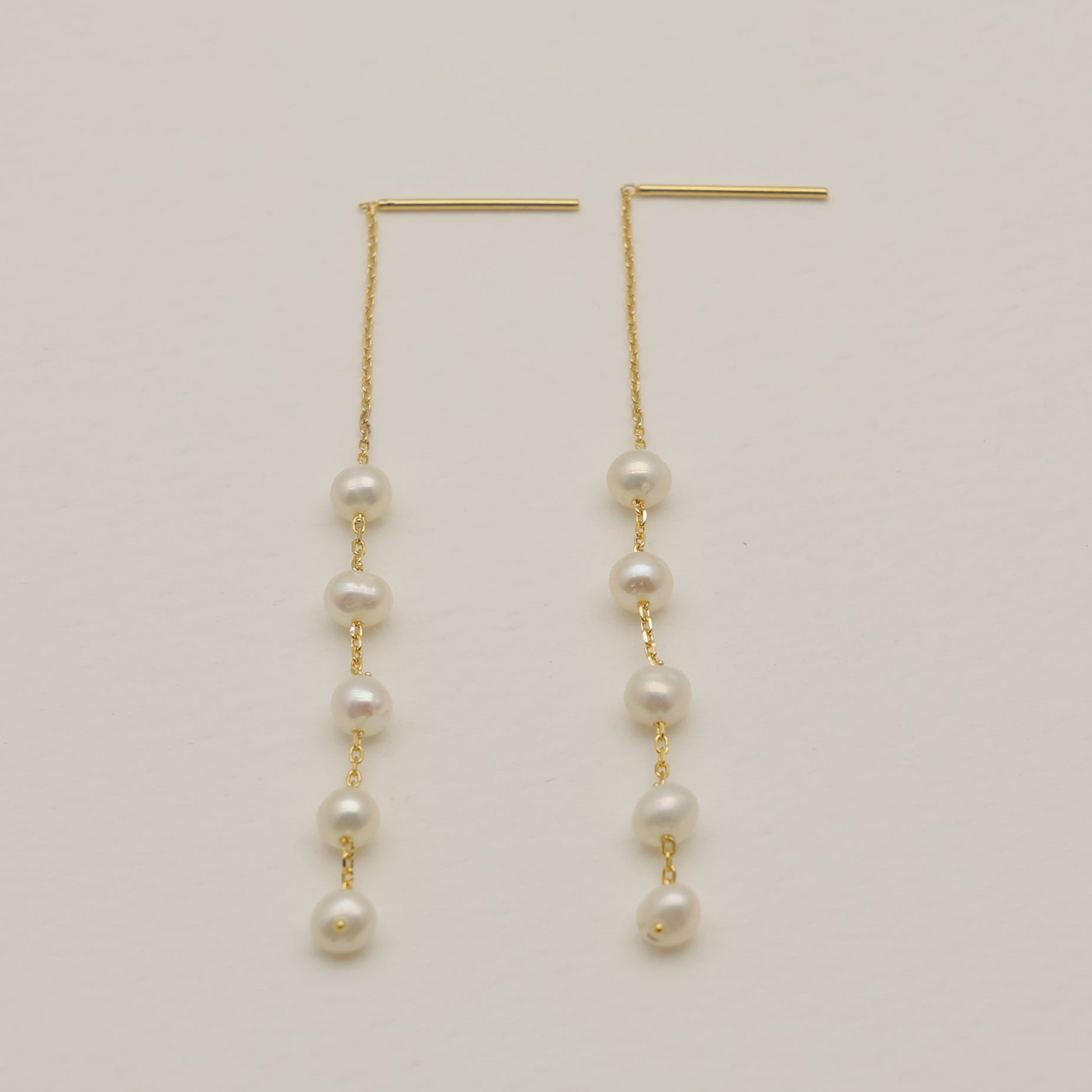 Gold earrings with pearl beads on a light beige background