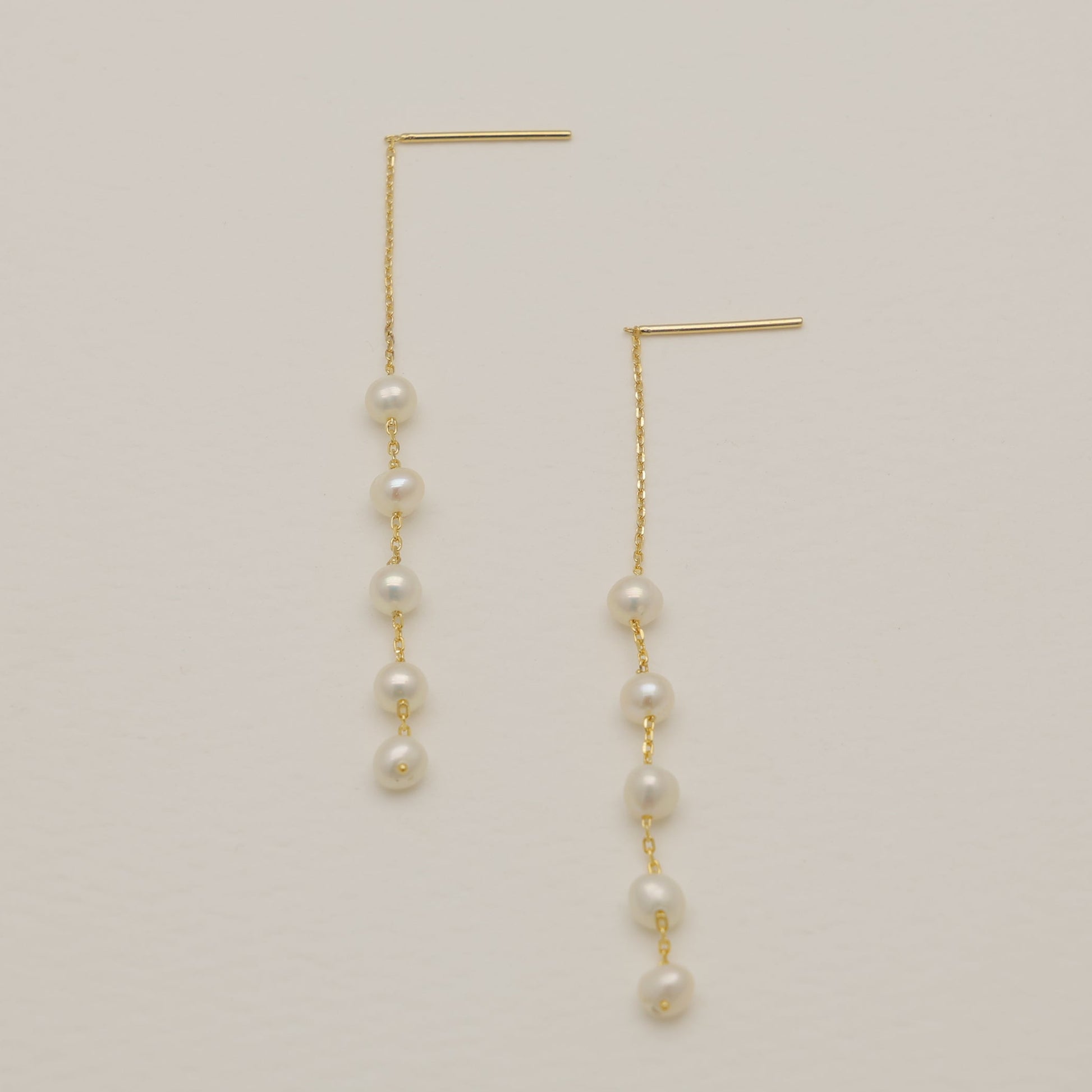Gold earrings with pearls on a beige background