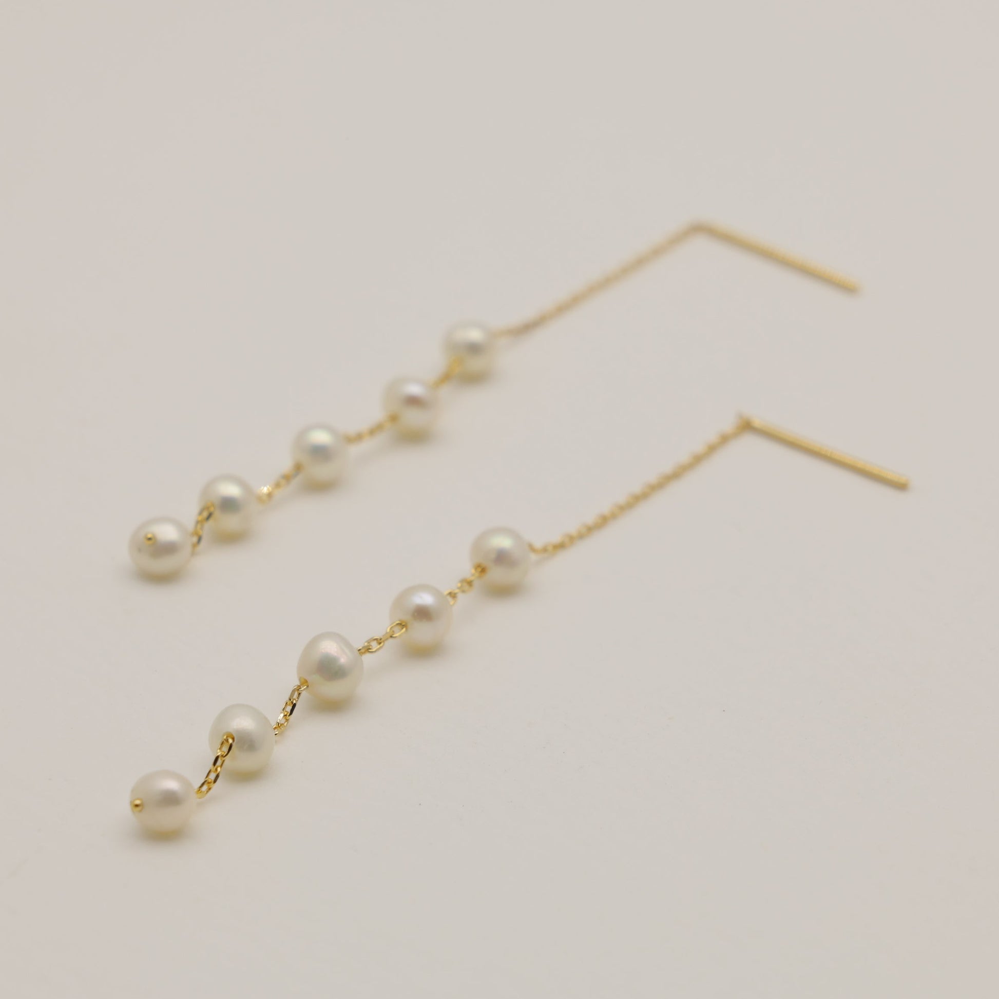 Pearl drop earrings on a light beige background