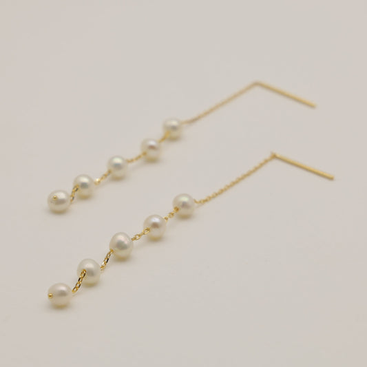 Pearl drop earrings on a light beige background