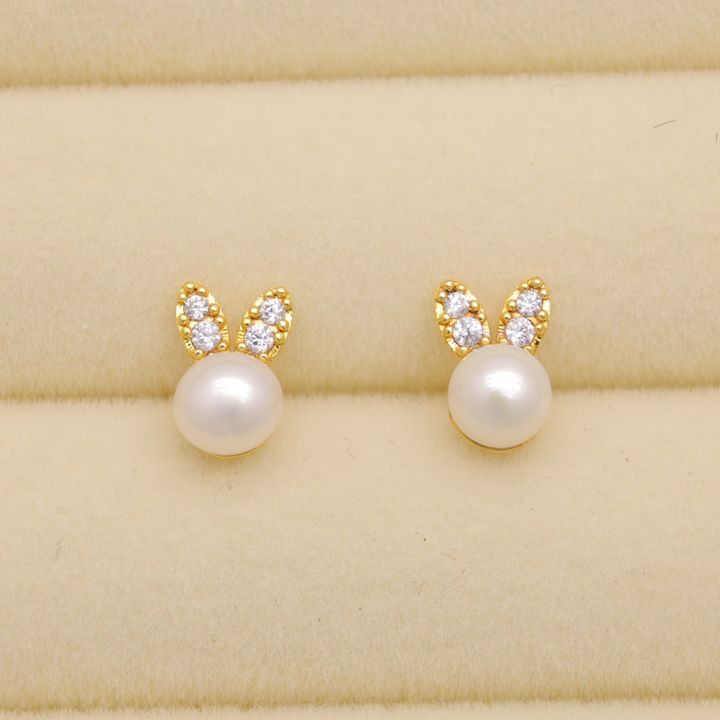 Pair of pearl earrings with gold bunny ears on a beige fabric background