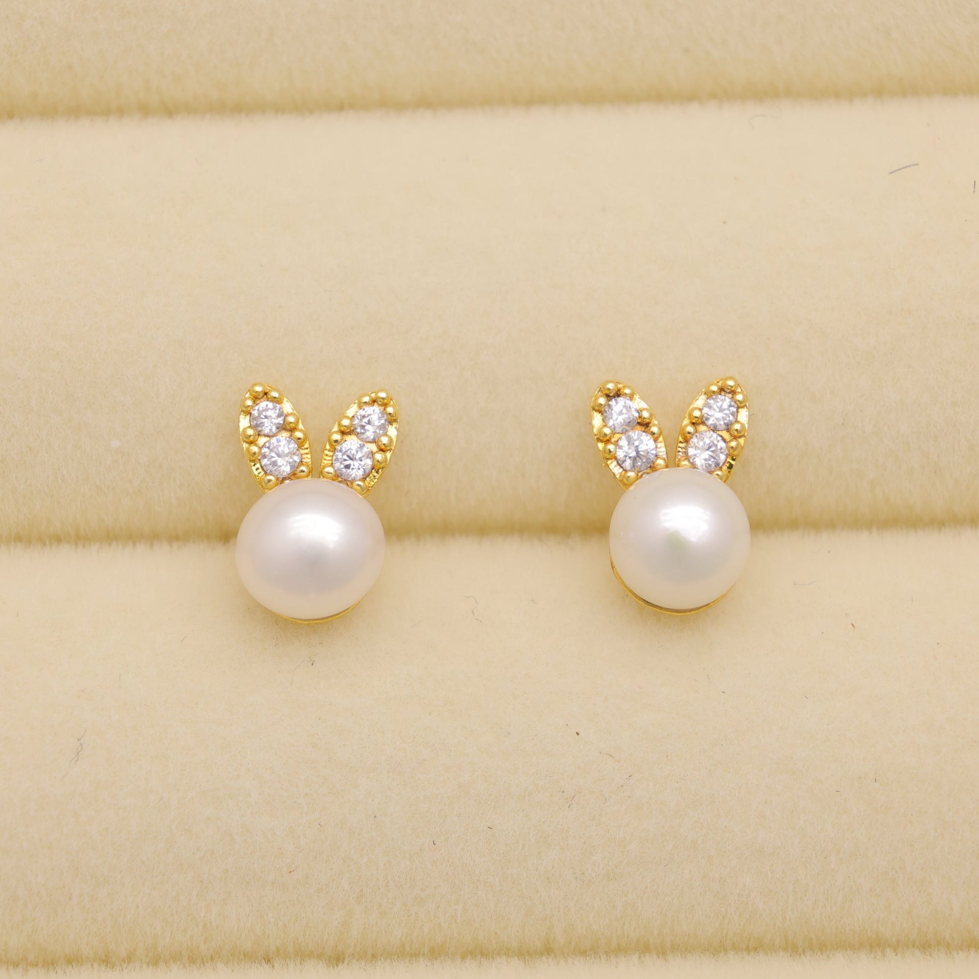 Pair of pearl earrings with gold bunny ears on a beige fabric background
