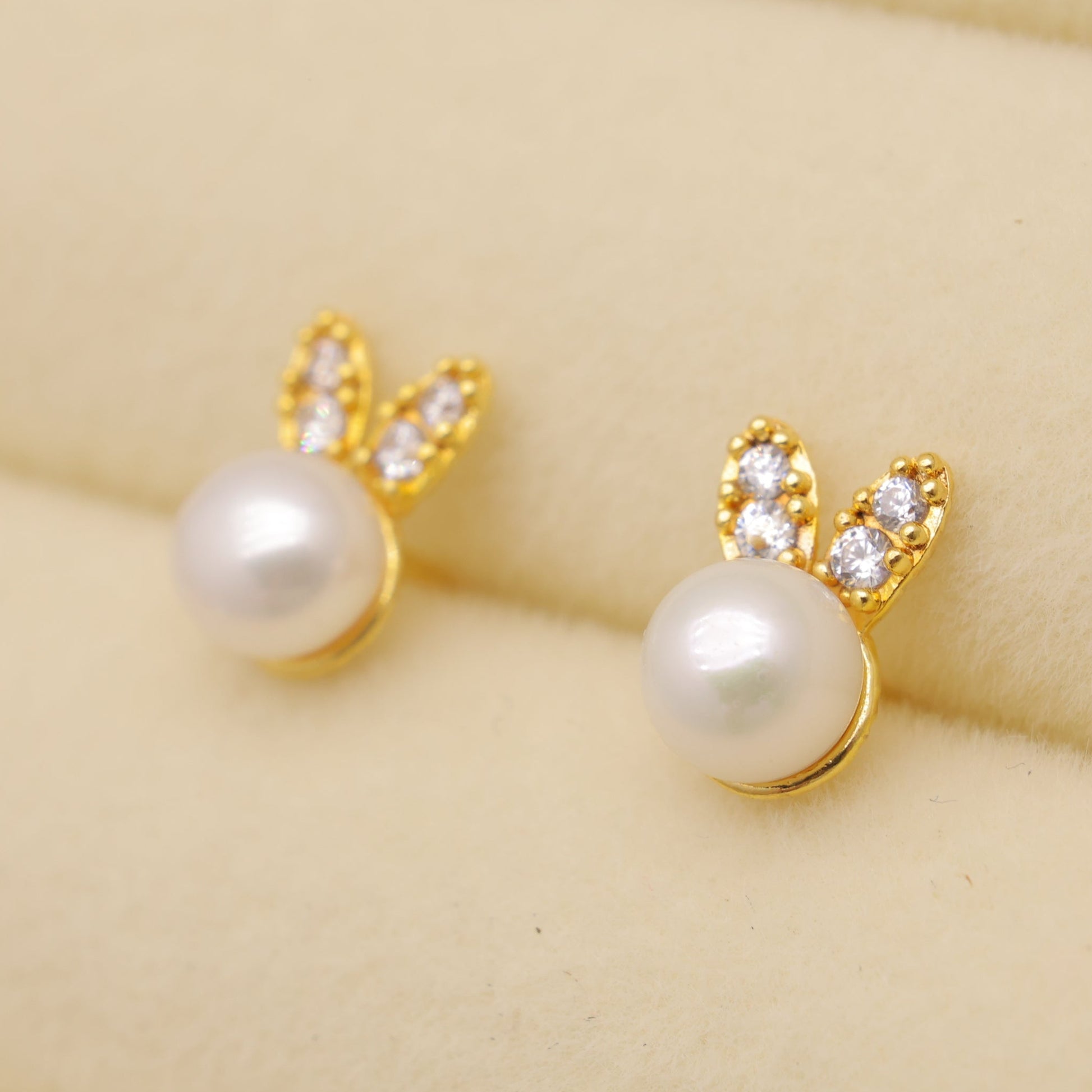 Gold earrings with pearl-like beads on a beige background