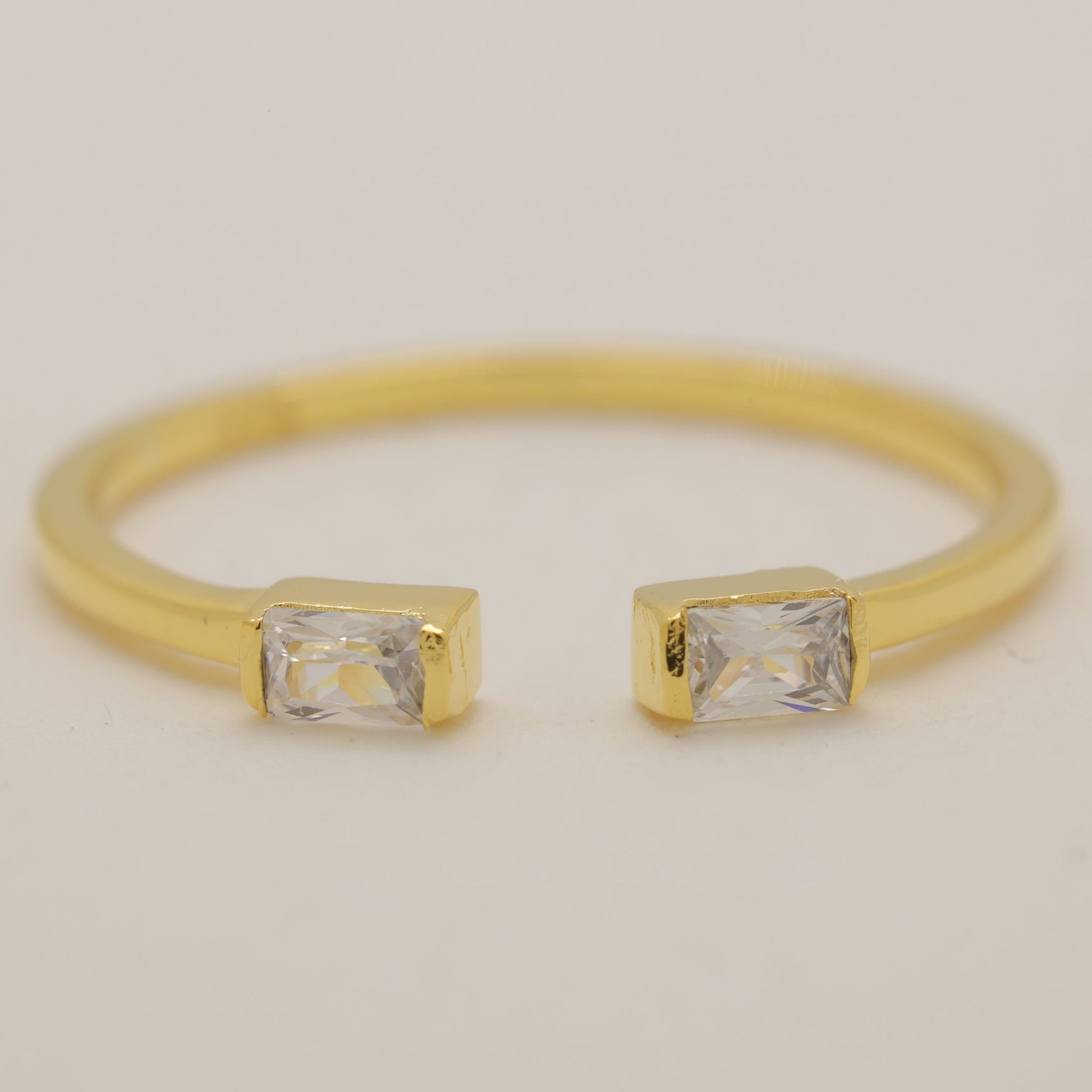 Gold ring with two rectangular gemstones on a light beige background