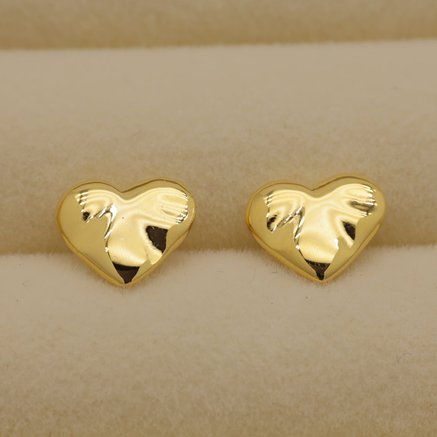 Gold heart-shaped earrings on a beige background
