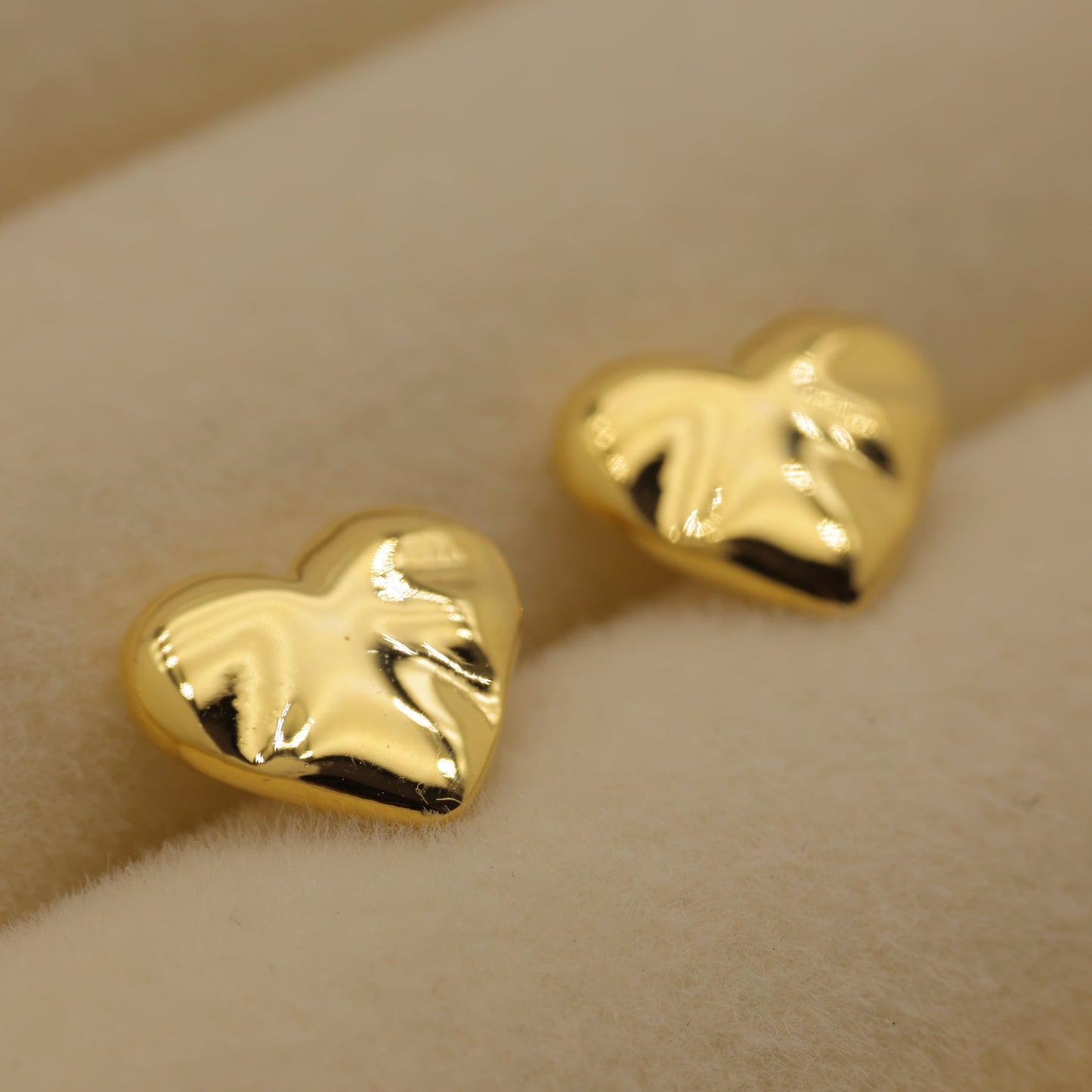 Gold heart-shaped earrings on a beige background