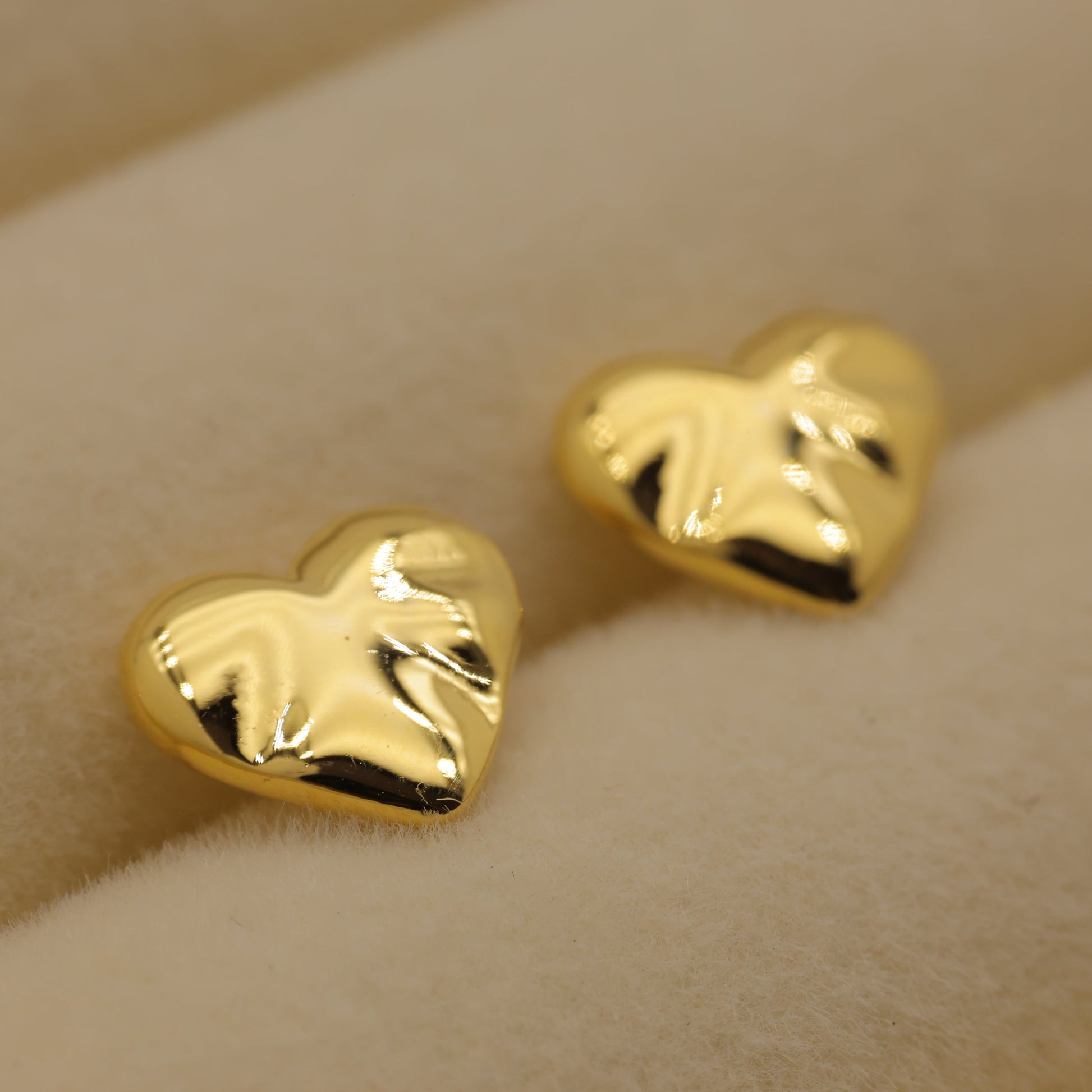 Gold heart-shaped earrings on a beige background