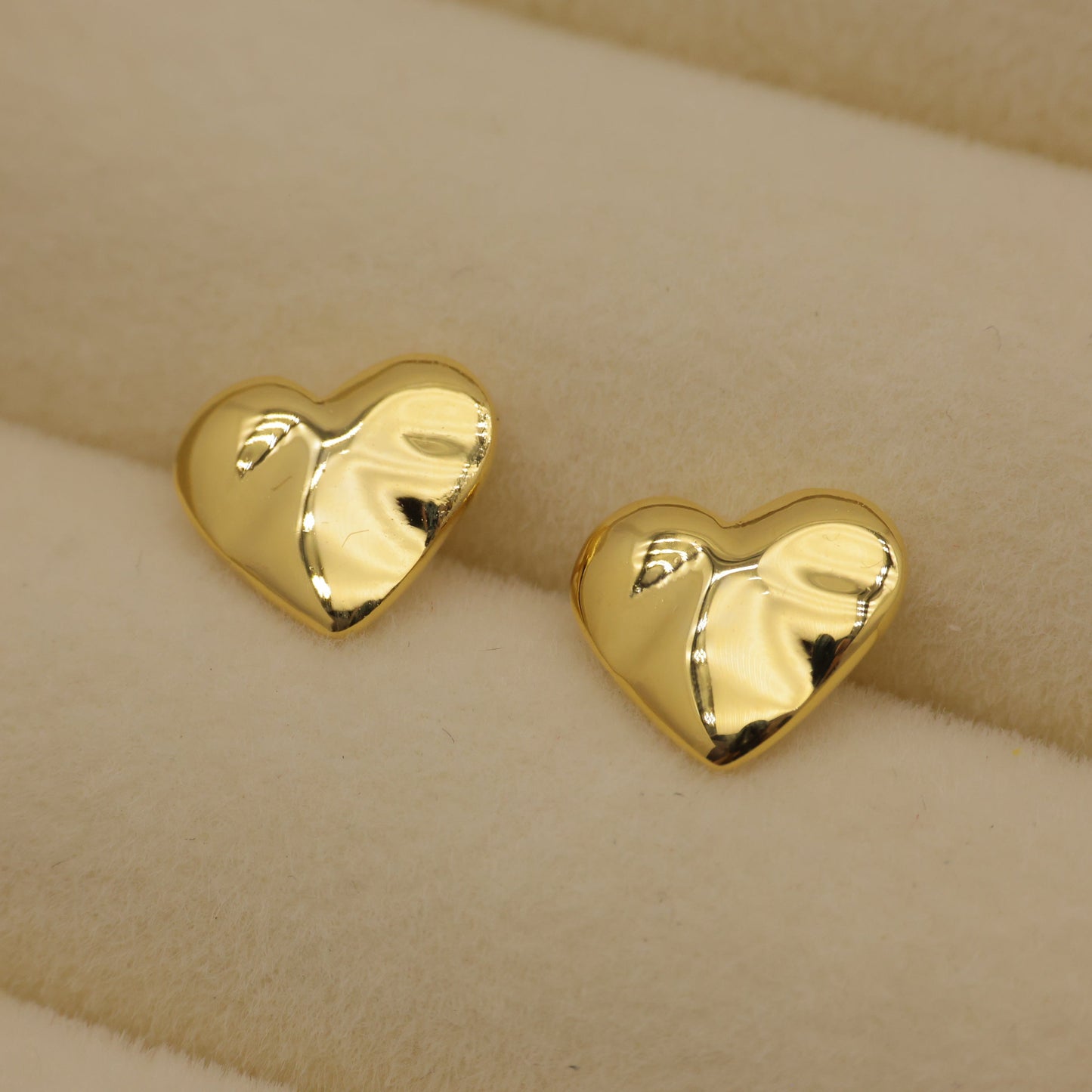 Gold heart-shaped earrings on a beige background