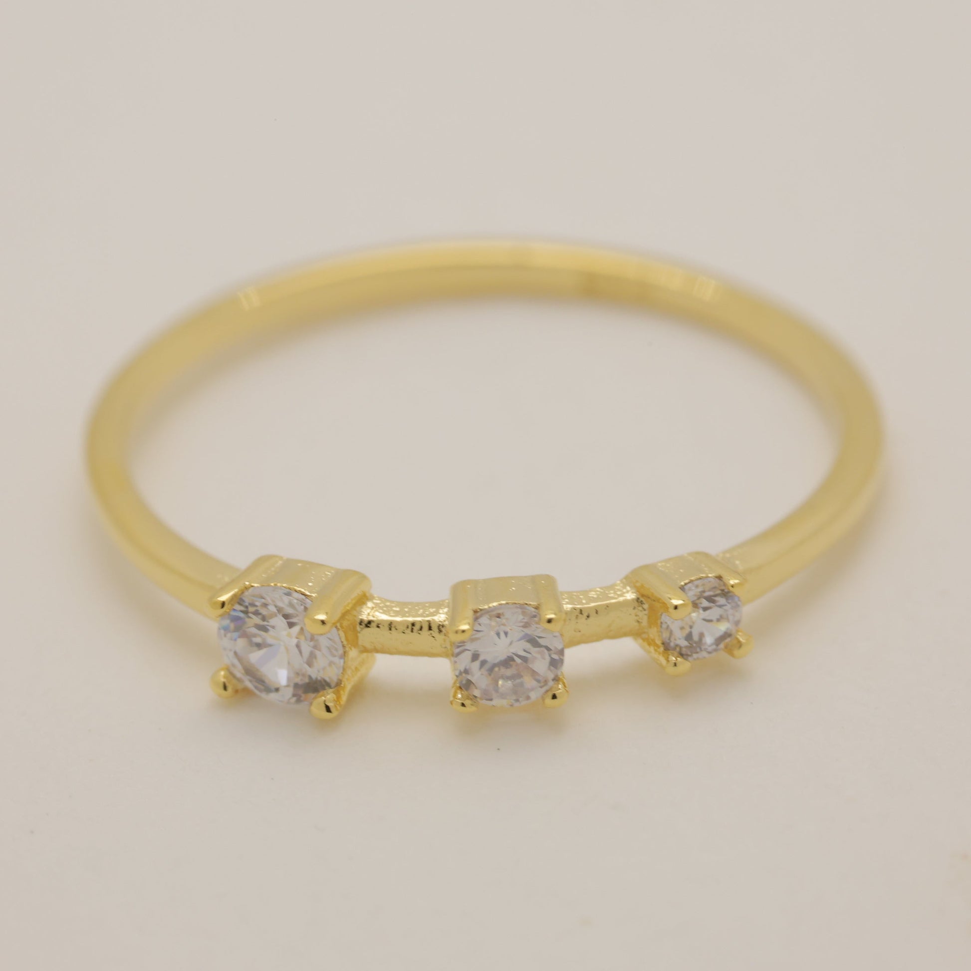 Gold ring with three diamonds on a light gray background