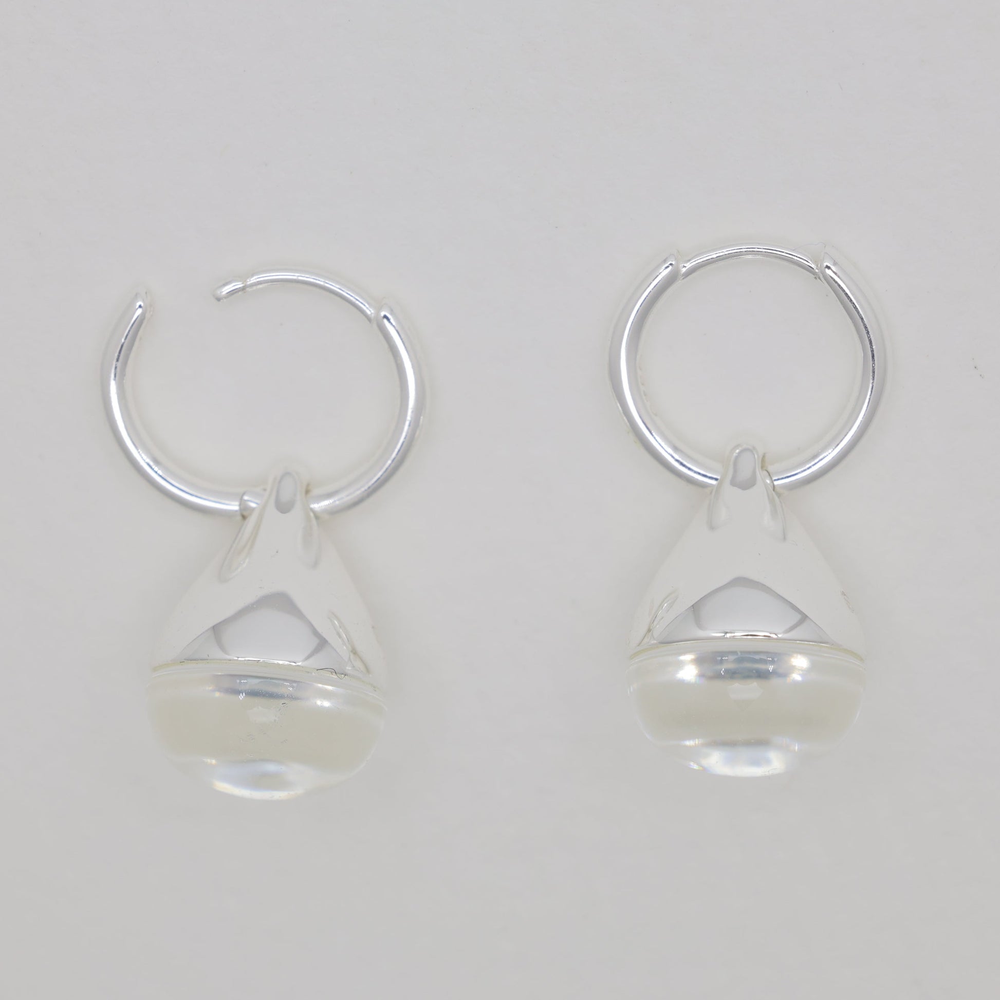 Pair of silver hoop earrings with clear teardrop-shaped charms on a light gray background