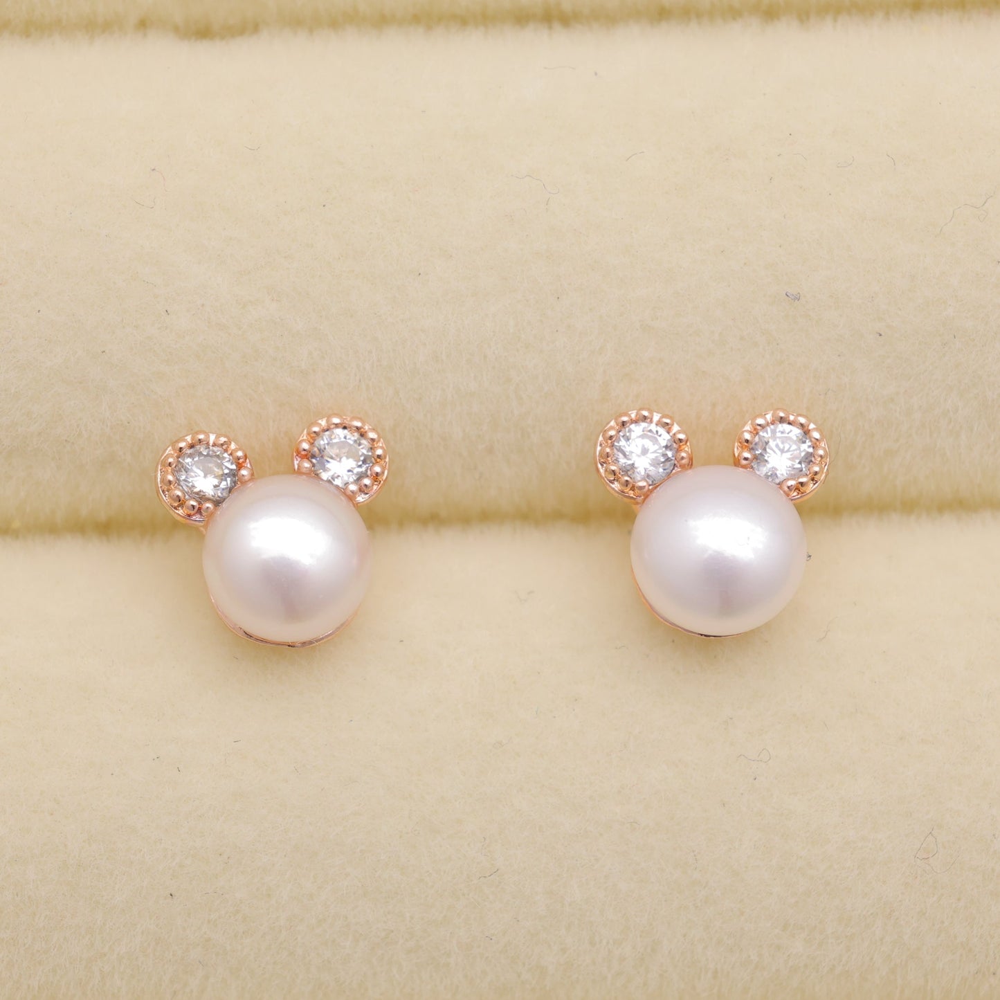 Pearl earrings with rose gold accents on a beige background