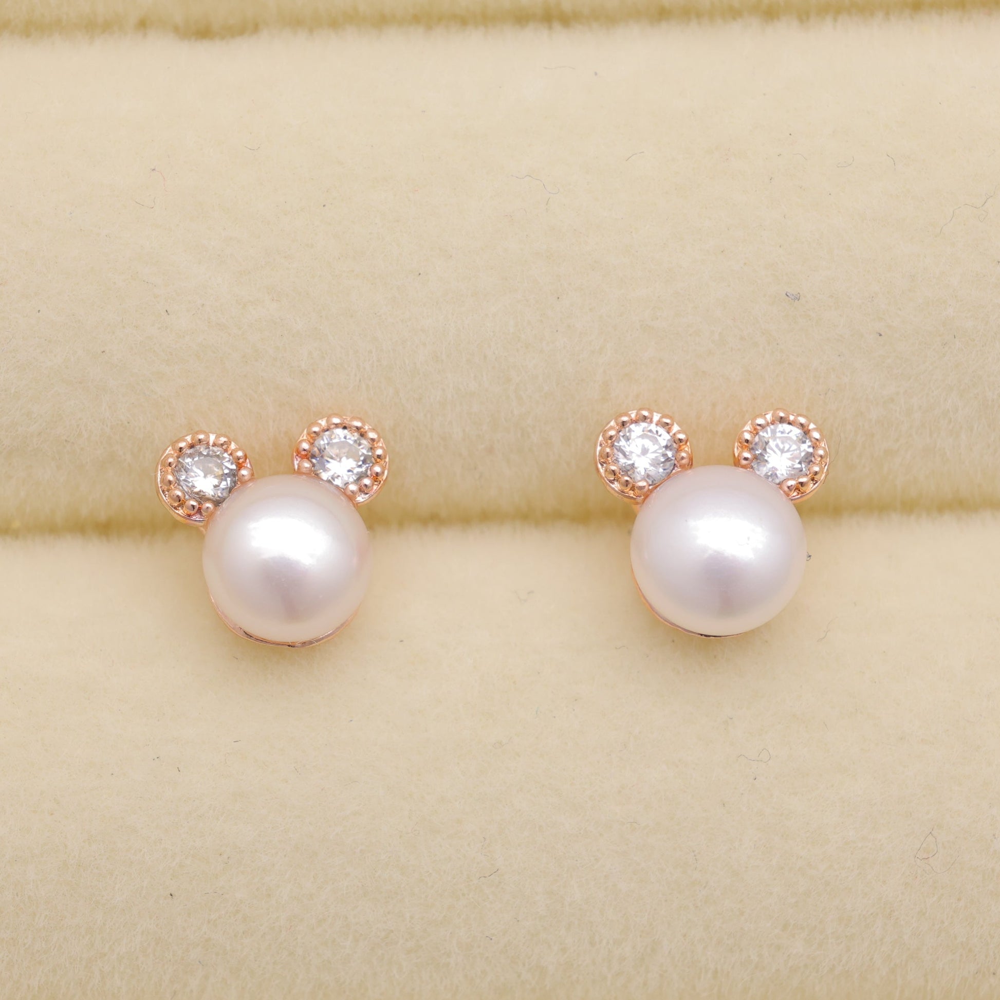 Pearl earrings with rose gold accents on a beige background