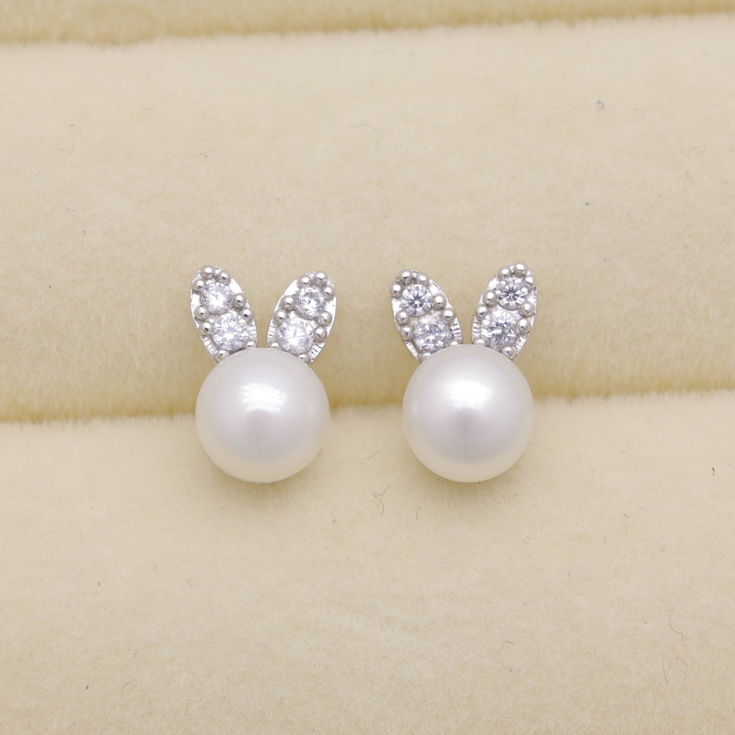 Pearl earrings with silver bunny ears on a beige background