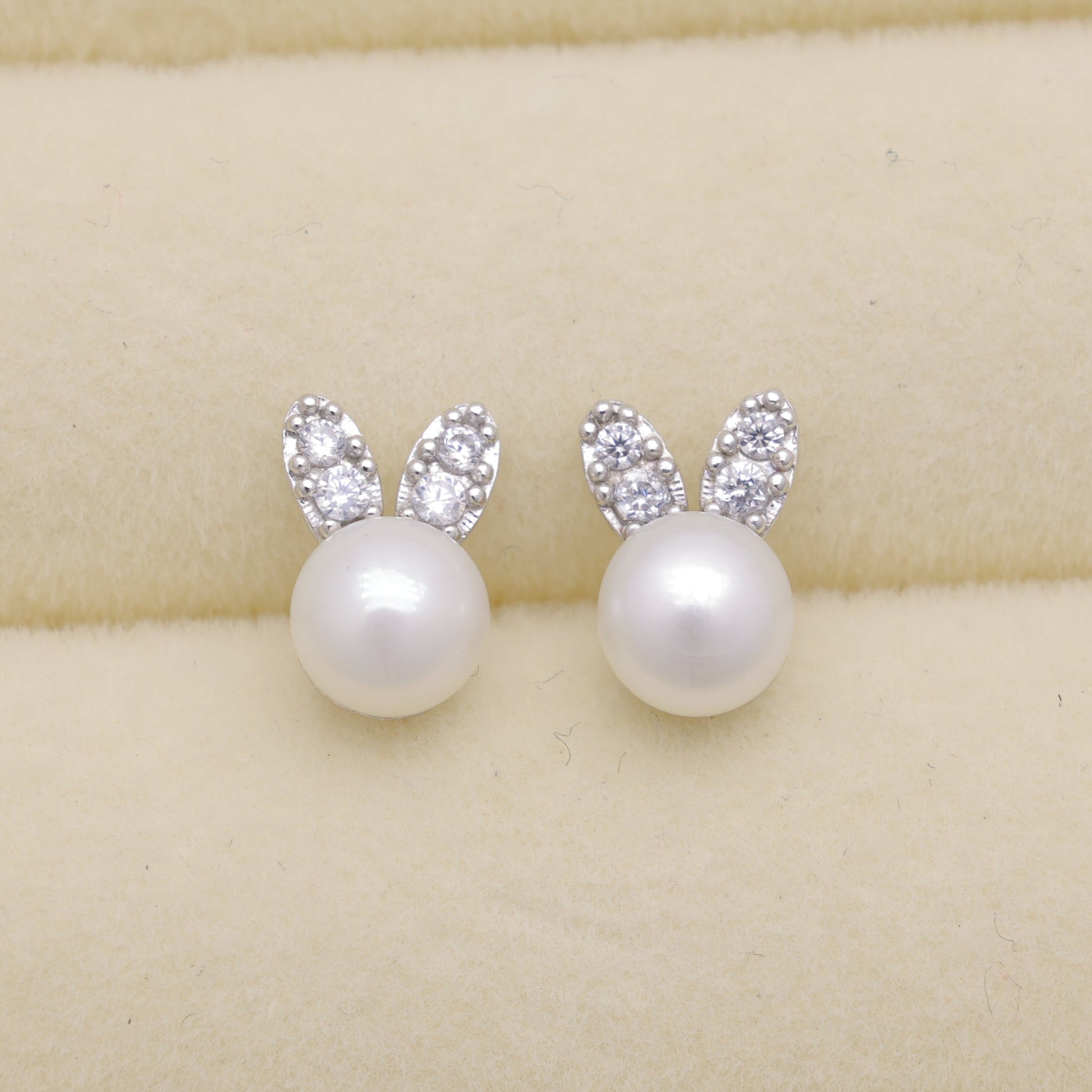 Pearl earrings with silver bunny ears on a beige background