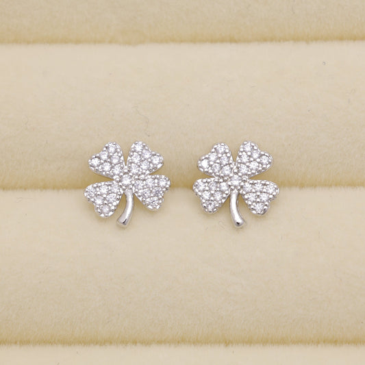 Silver shamrock earrings on a beige wooden surface