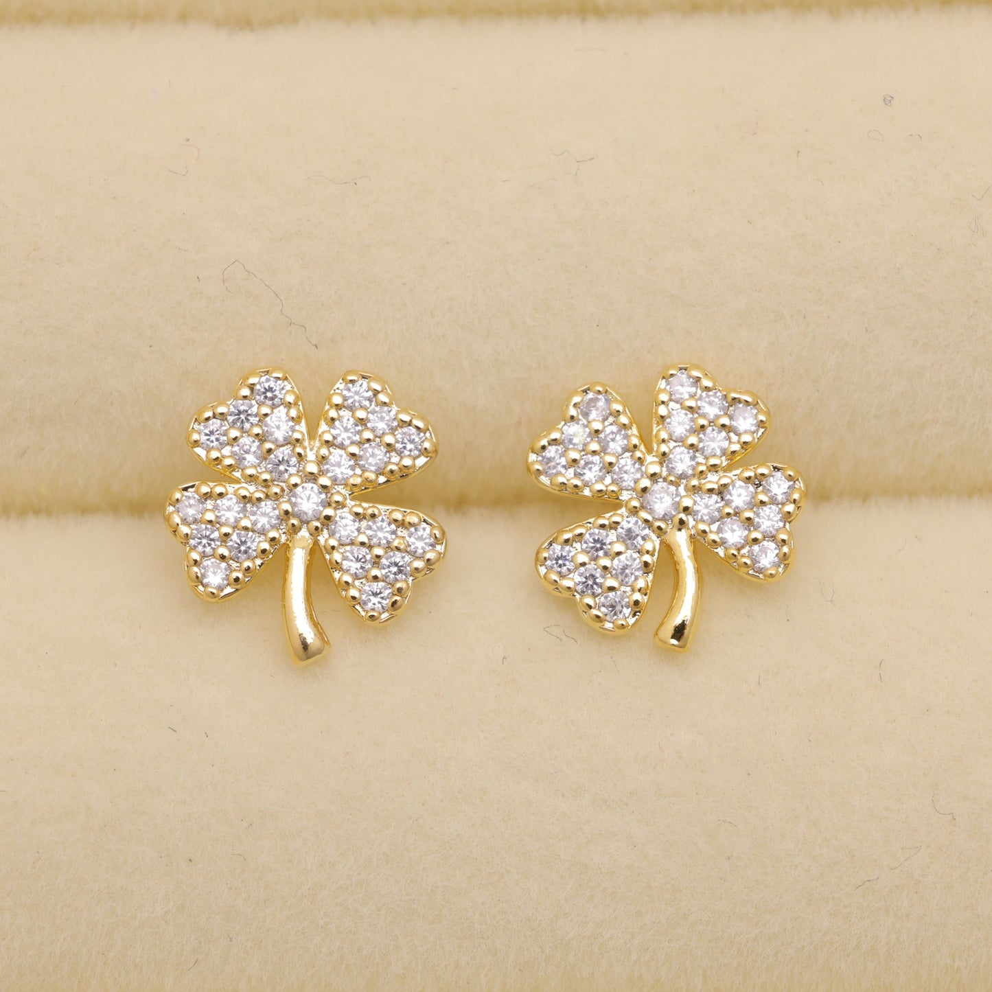Gold shamrock earrings with clear stones on a beige background