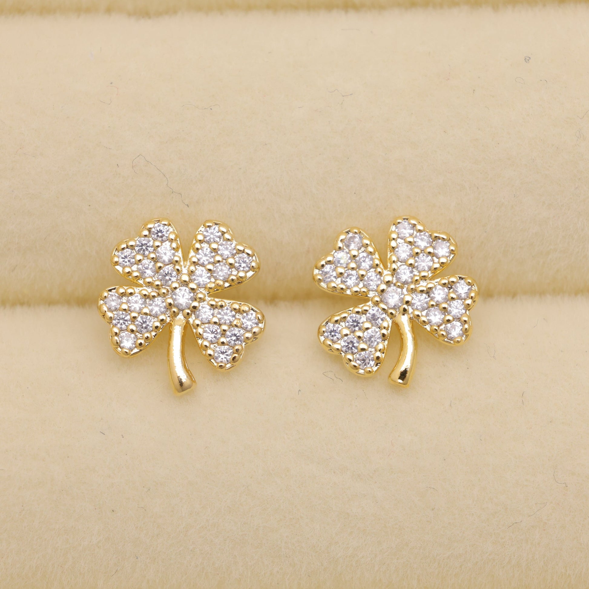 Gold shamrock earrings with clear stones on a beige background