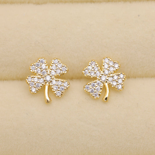 Gold shamrock earrings with clear stones on a beige background