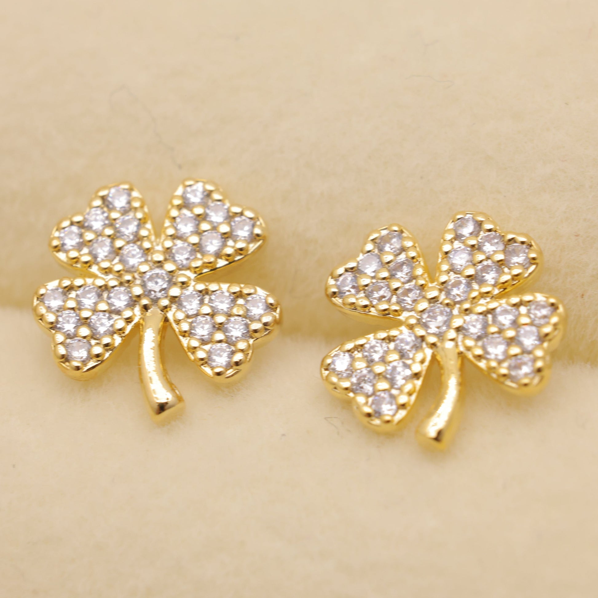 Gold four-leaf clover earrings with clear stones on a beige background