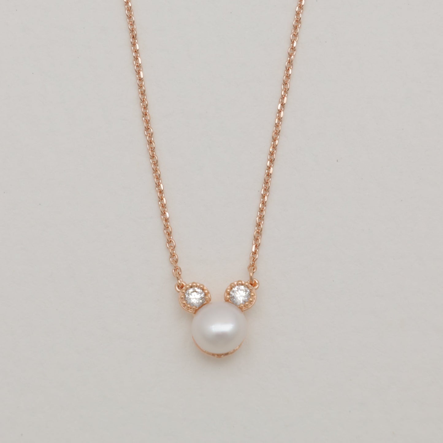 Pearl necklace with rose gold chain on a light gray background