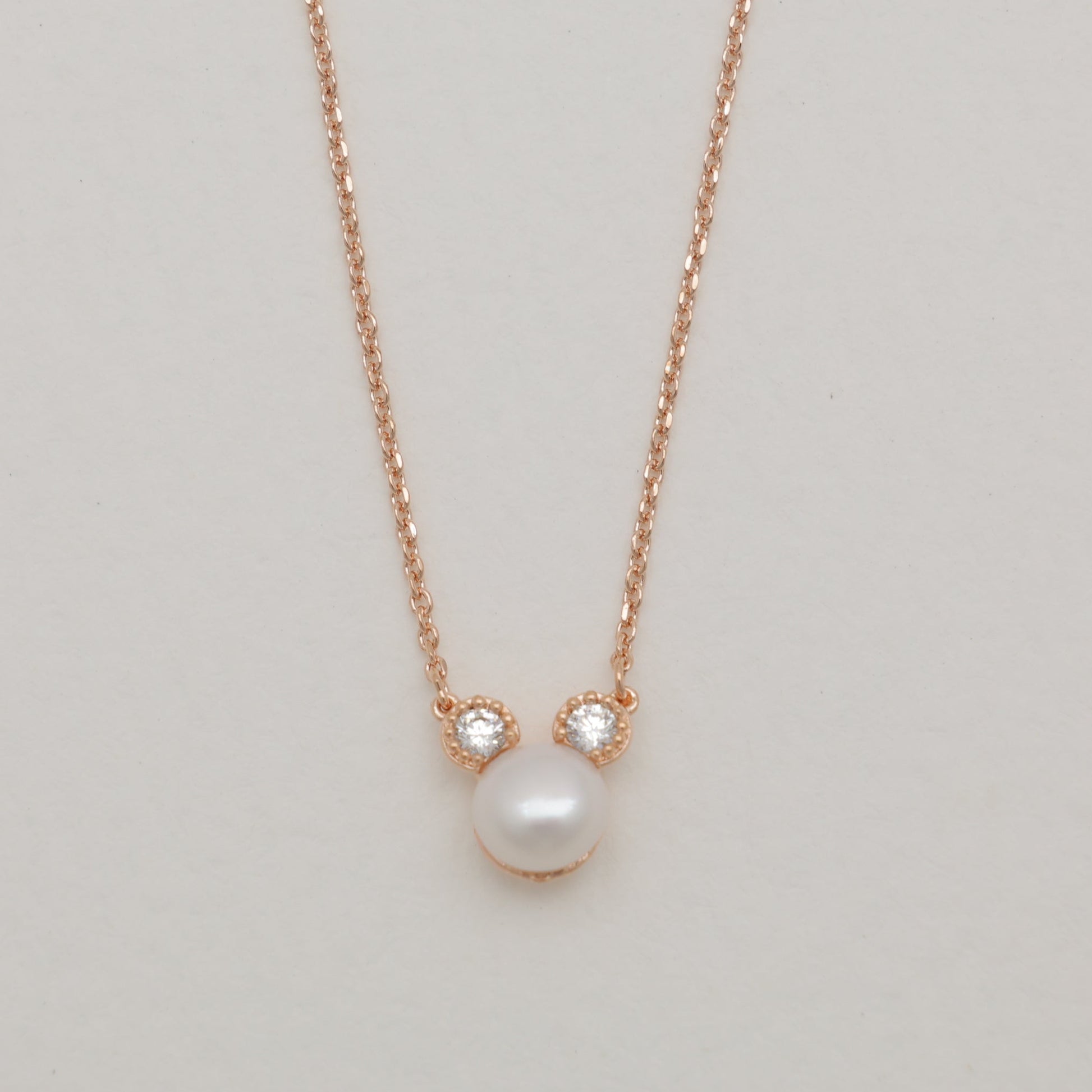 Pearl necklace with rose gold chain on a light gray background