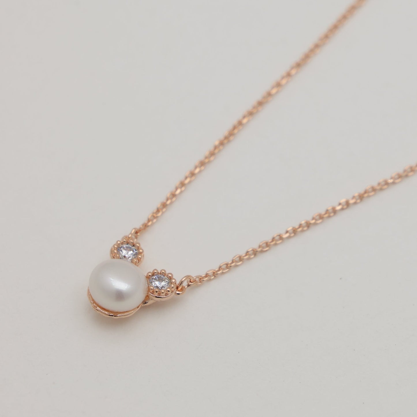 Pearl necklace with rose gold chain on a light gray background
